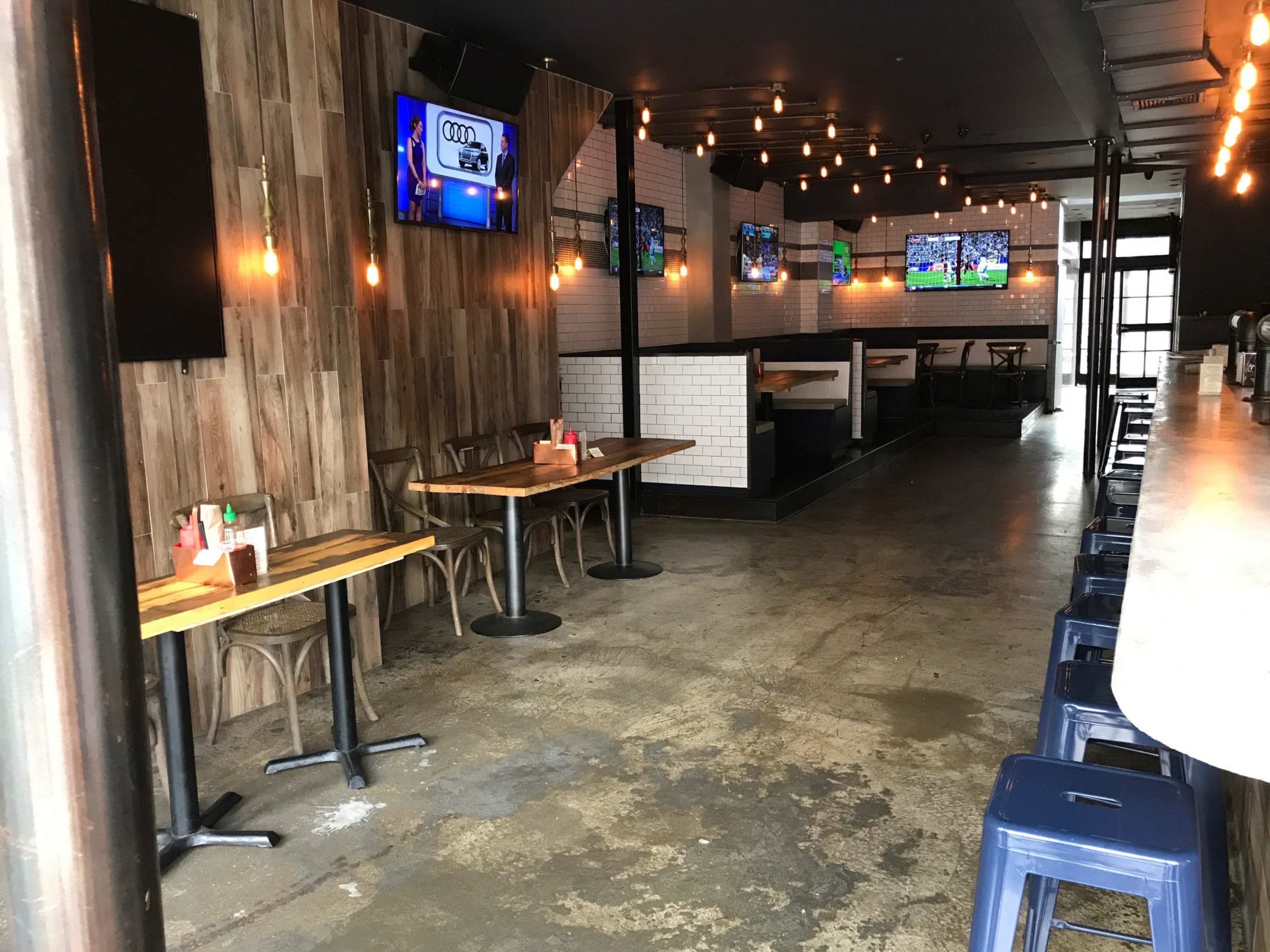 The interior of a bar features wooden walls, multiple television screens, and a mix of tables and bar seating.
