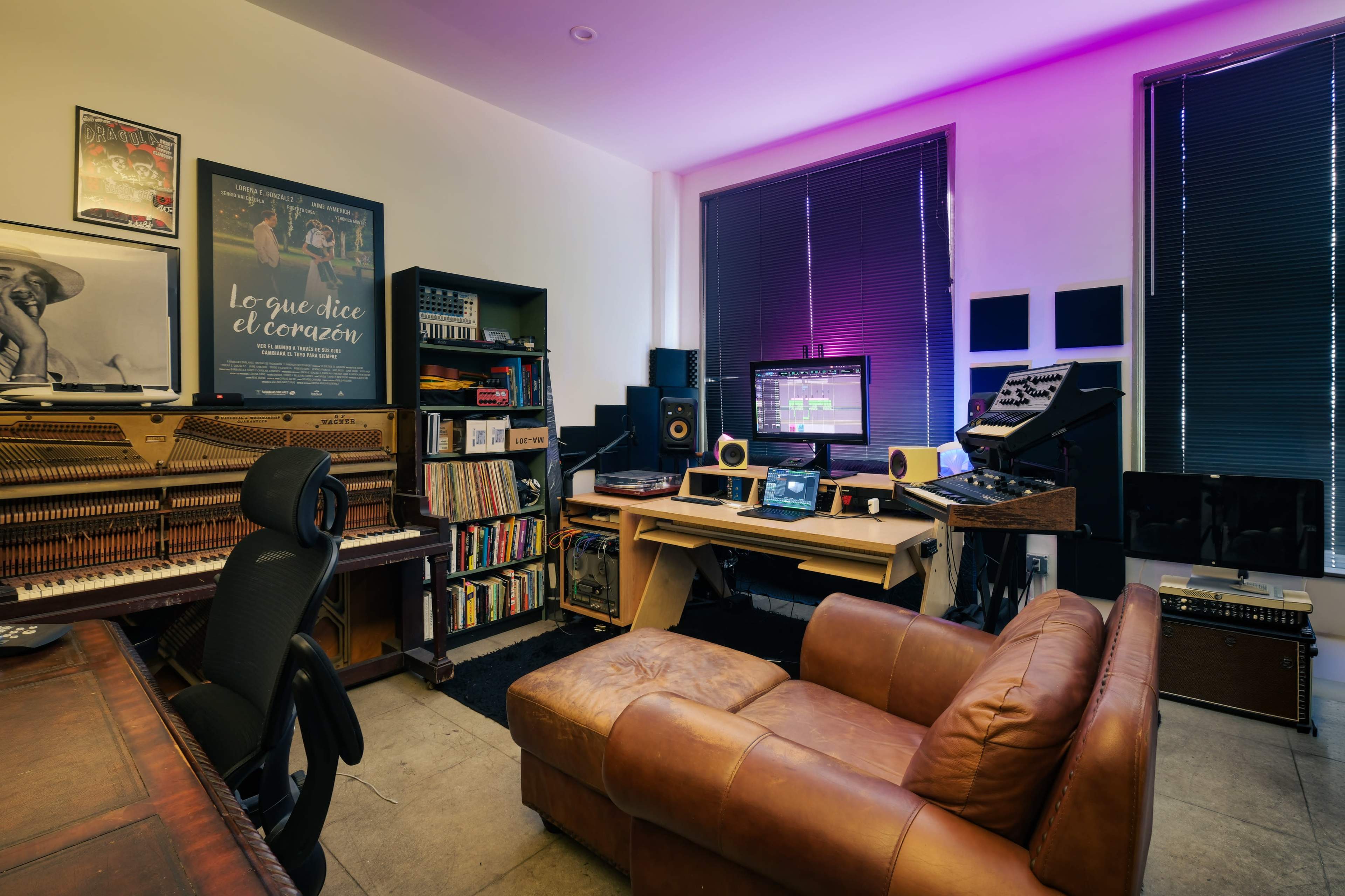 A music studio features a leather sofa, shelves of records, a desk with audio equipment, and screens displaying music software.