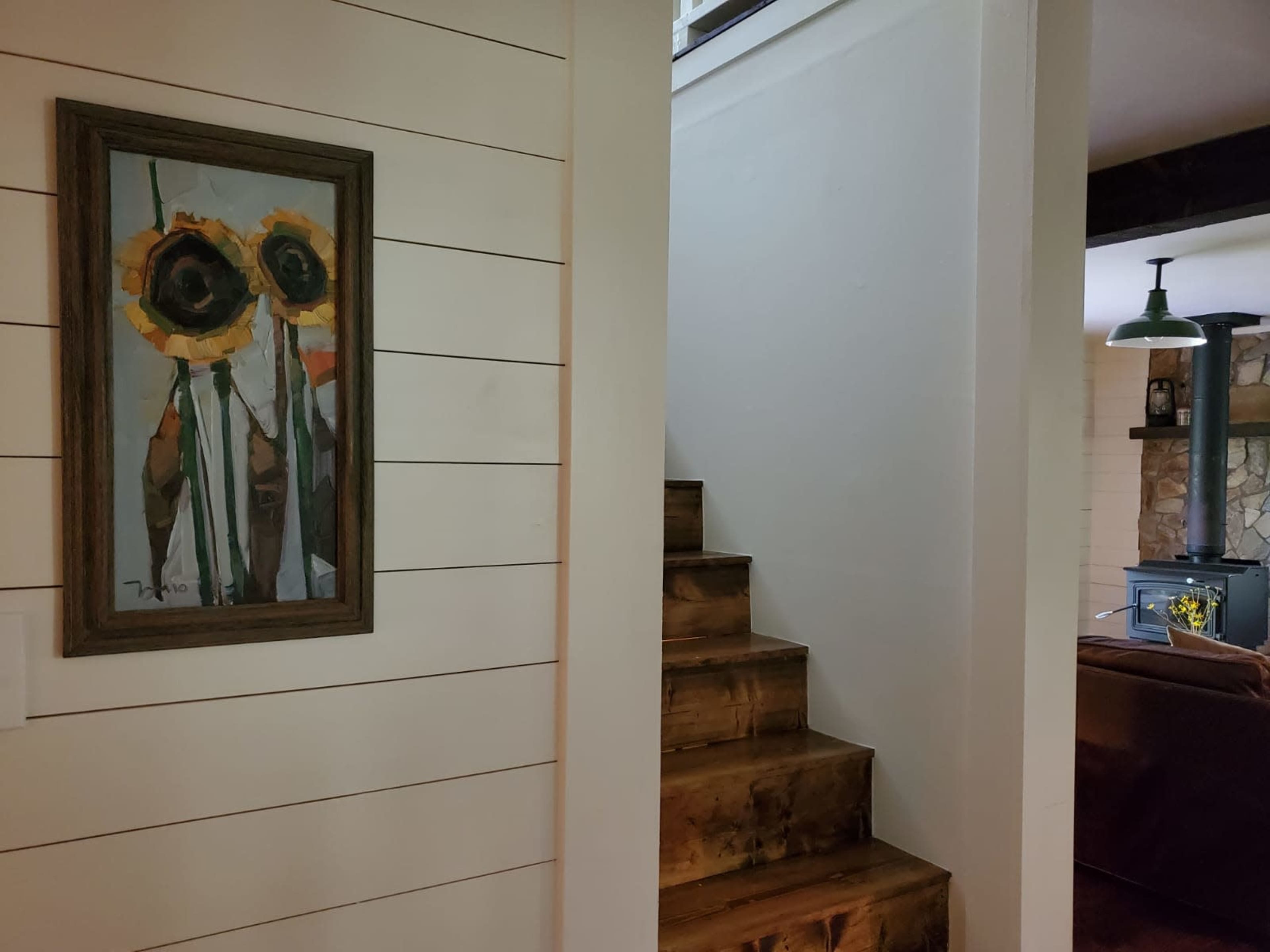 A framed painting of sunflowers hangs on a wall next to a set of wooden stairs leading to an upper level.