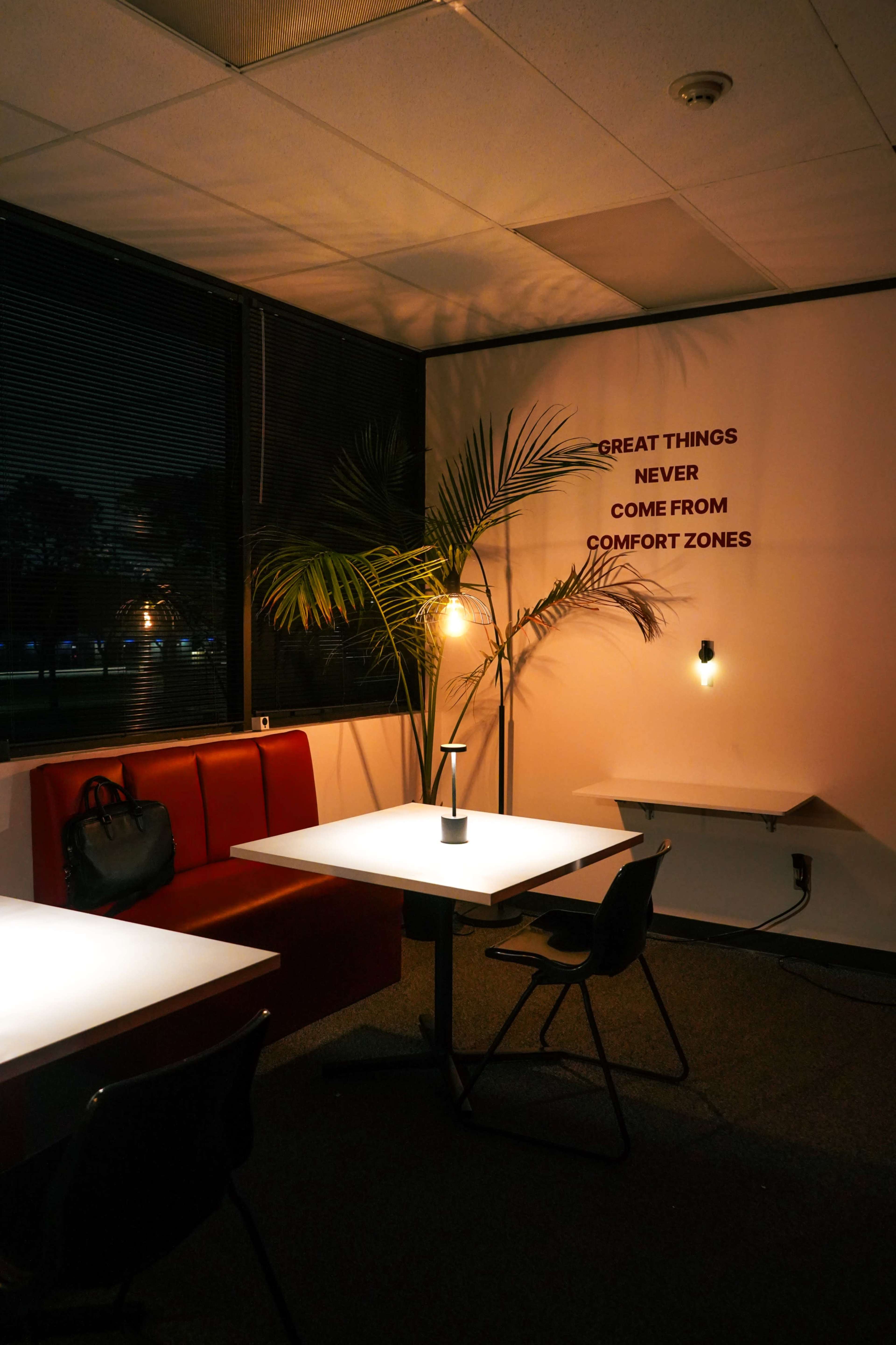 A dimly lit office space with red seating, white tables, and a wall displaying motivational text.