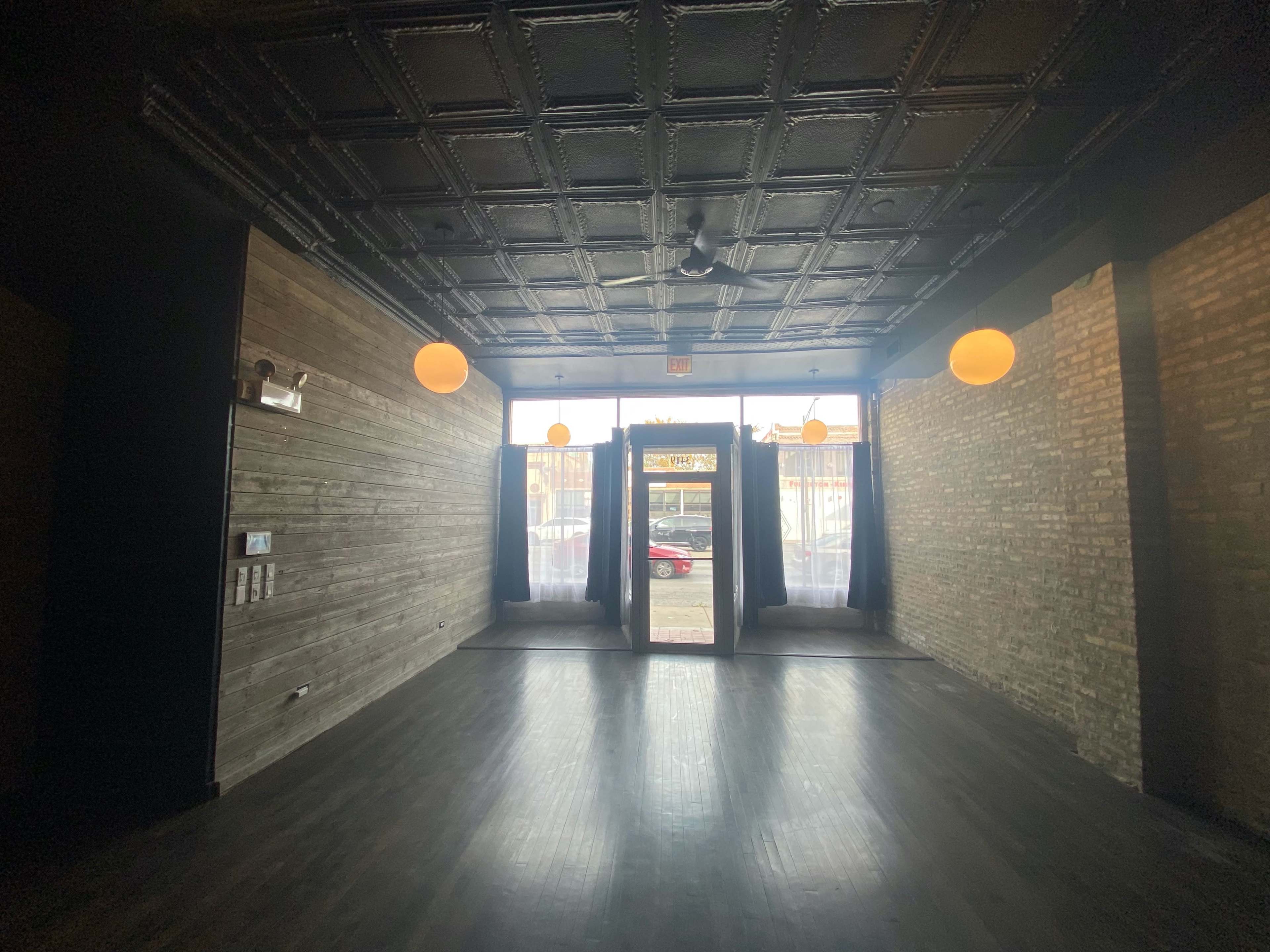 An empty room with a black ceiling, wooden walls, and a doorway flanked by dark curtains, leading to a bright exterior space.