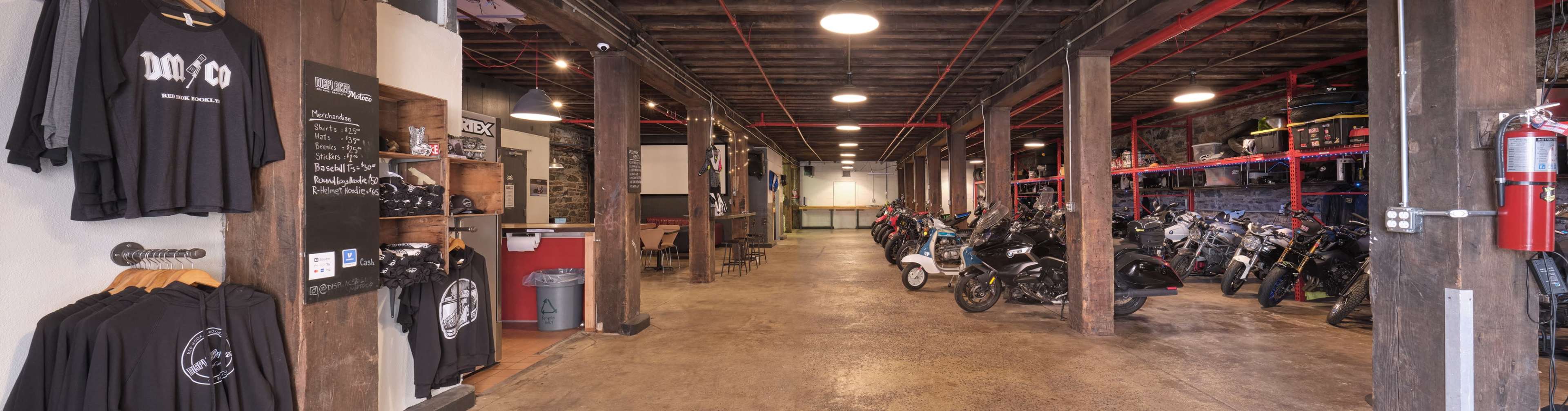 A spacious interior of a motorcycle shop with clothing displays on one side and a row of parked motorcycles on the opposite side.