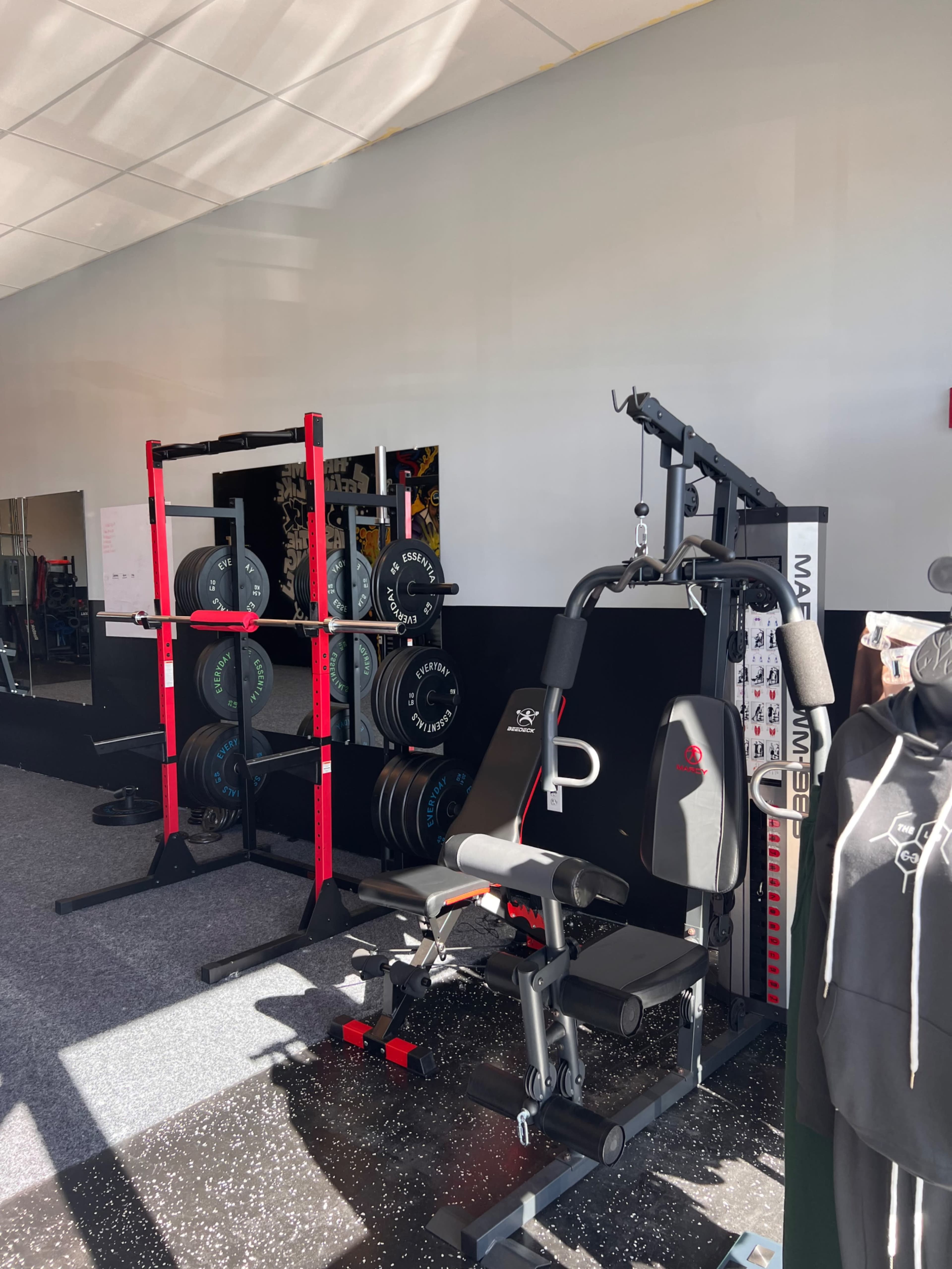 A gym interior with weightlifting equipment, including a squat rack and a multi-functional weight machine, along with various weights on a rack.