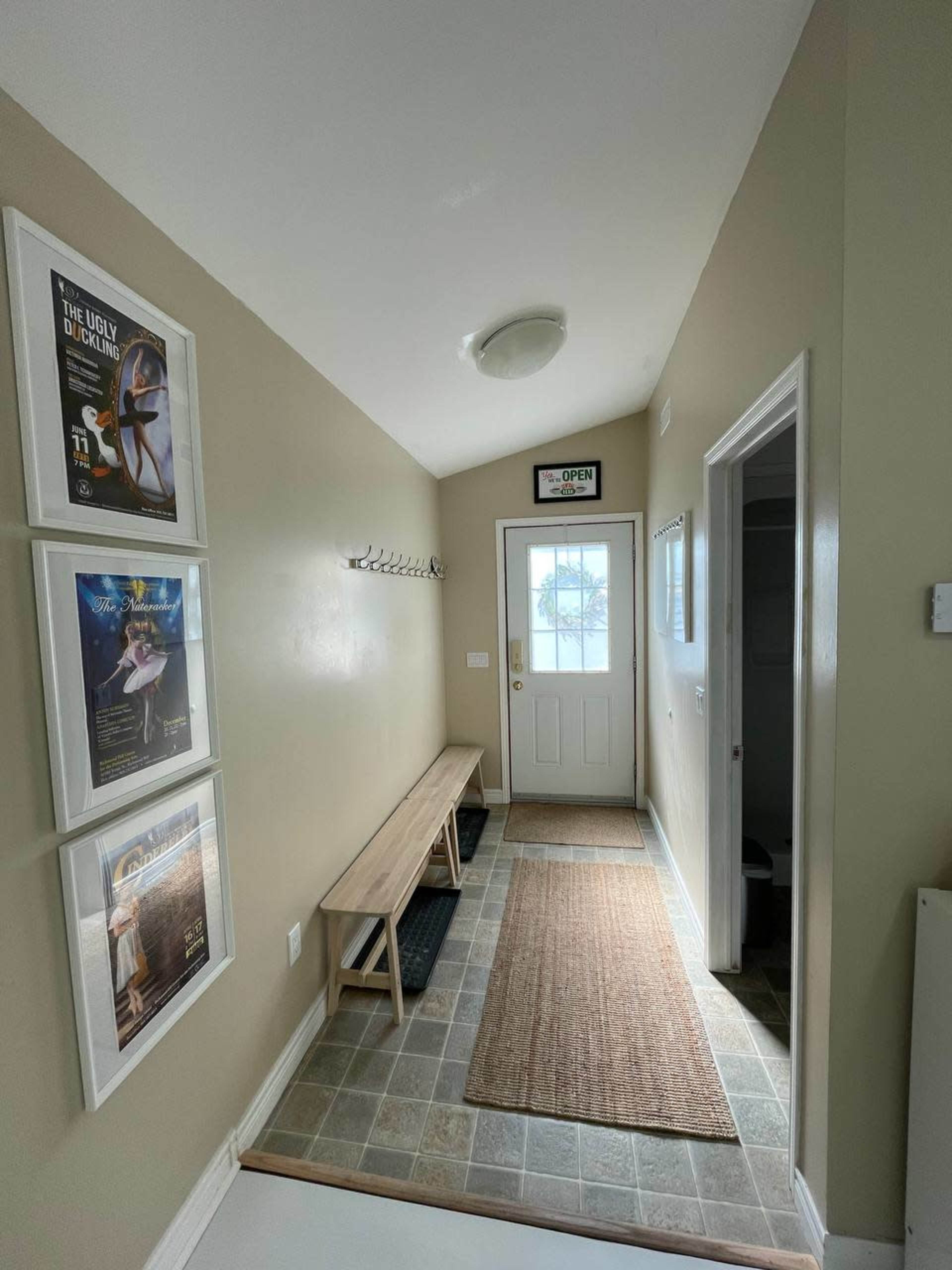 A narrow hallway with a bench, coat hooks, framed posters on the walls, and a door leading outside.