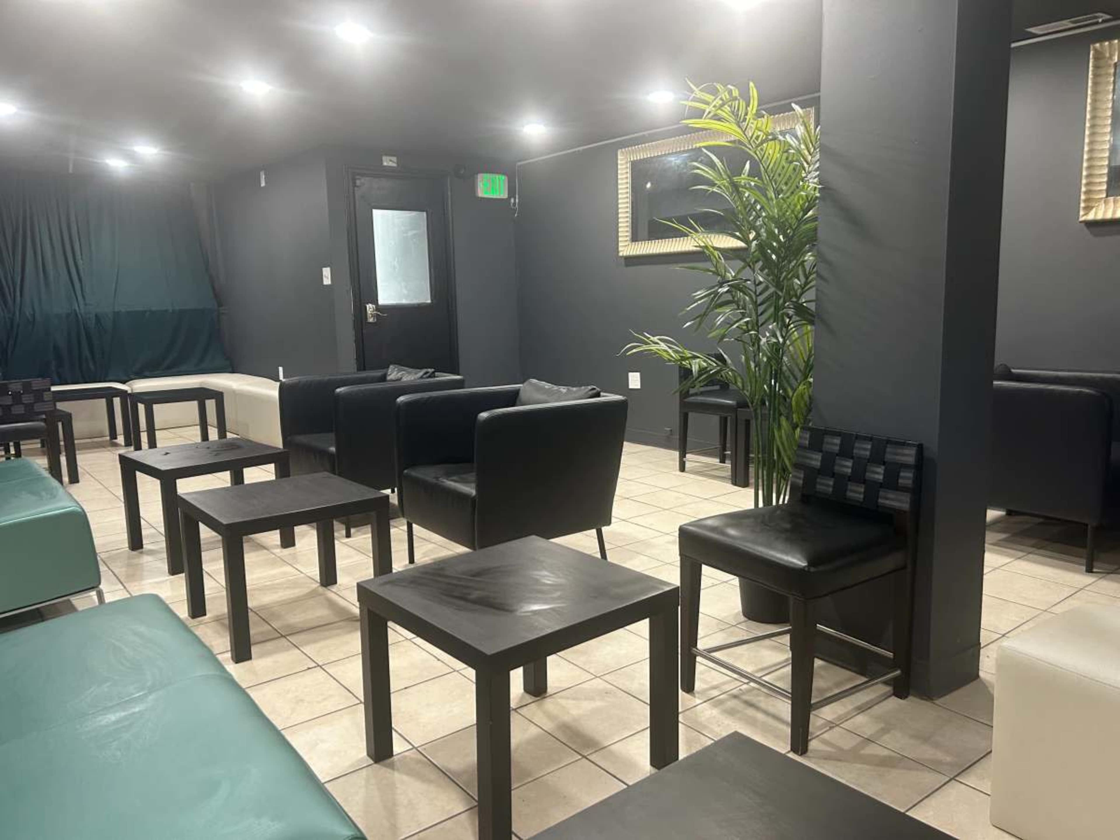 A modern lounge area with black and white furniture, including chairs and tables, against a backdrop of gray walls and dim lighting.