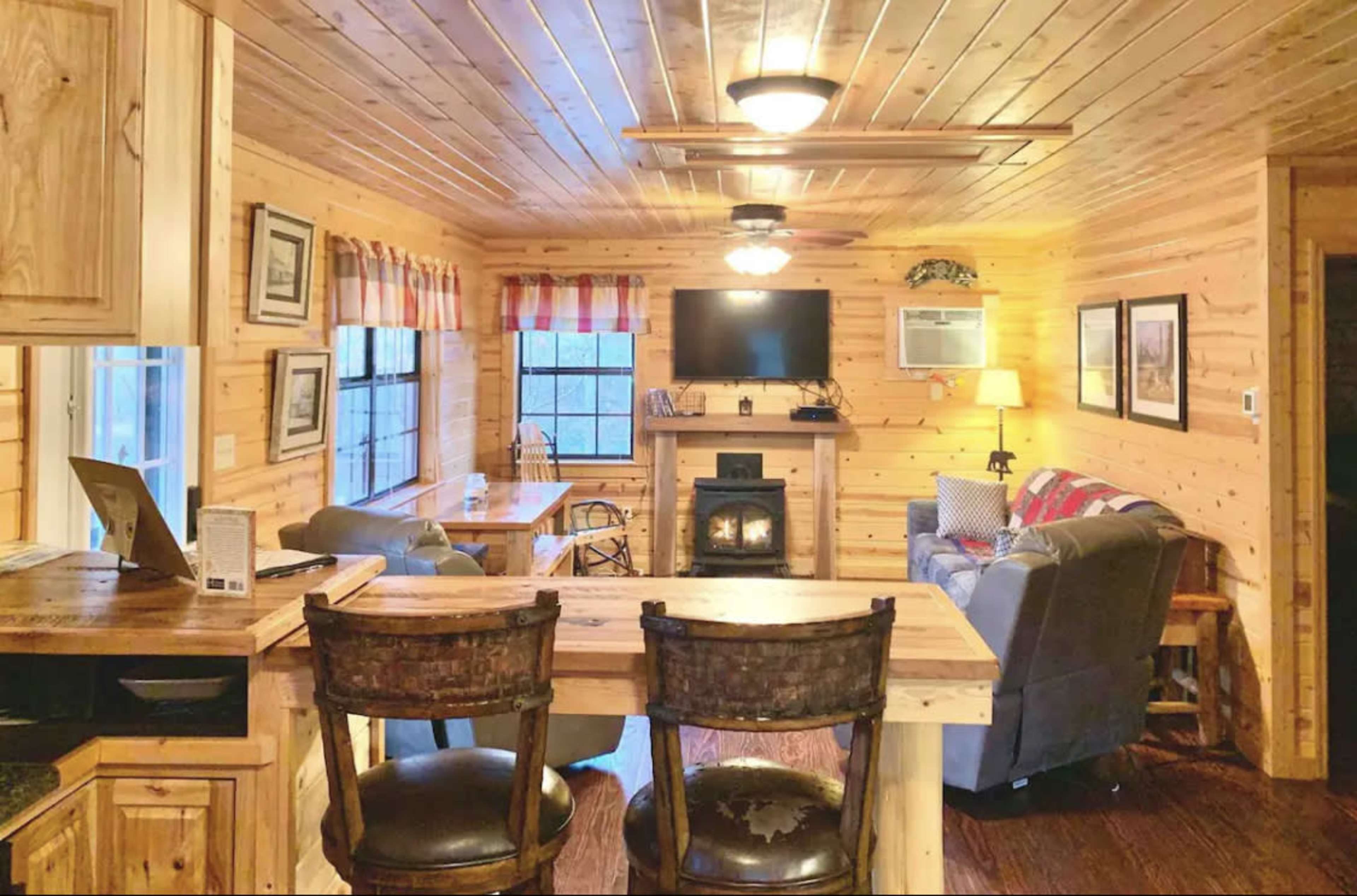 A wooden, rustic interior of a cabin with a living area, dining table, and a small fireplace.