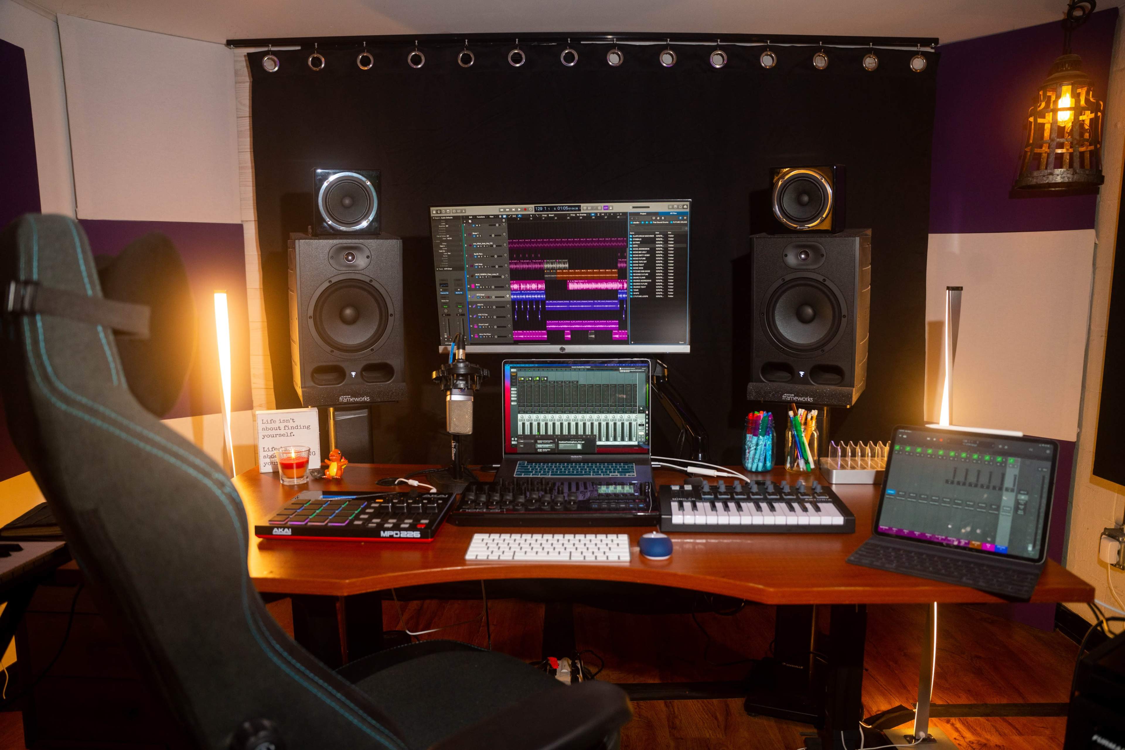 A modern music production studio setup featuring multiple computer monitors, audio speakers, a MIDI keyboard, and a swivel chair.