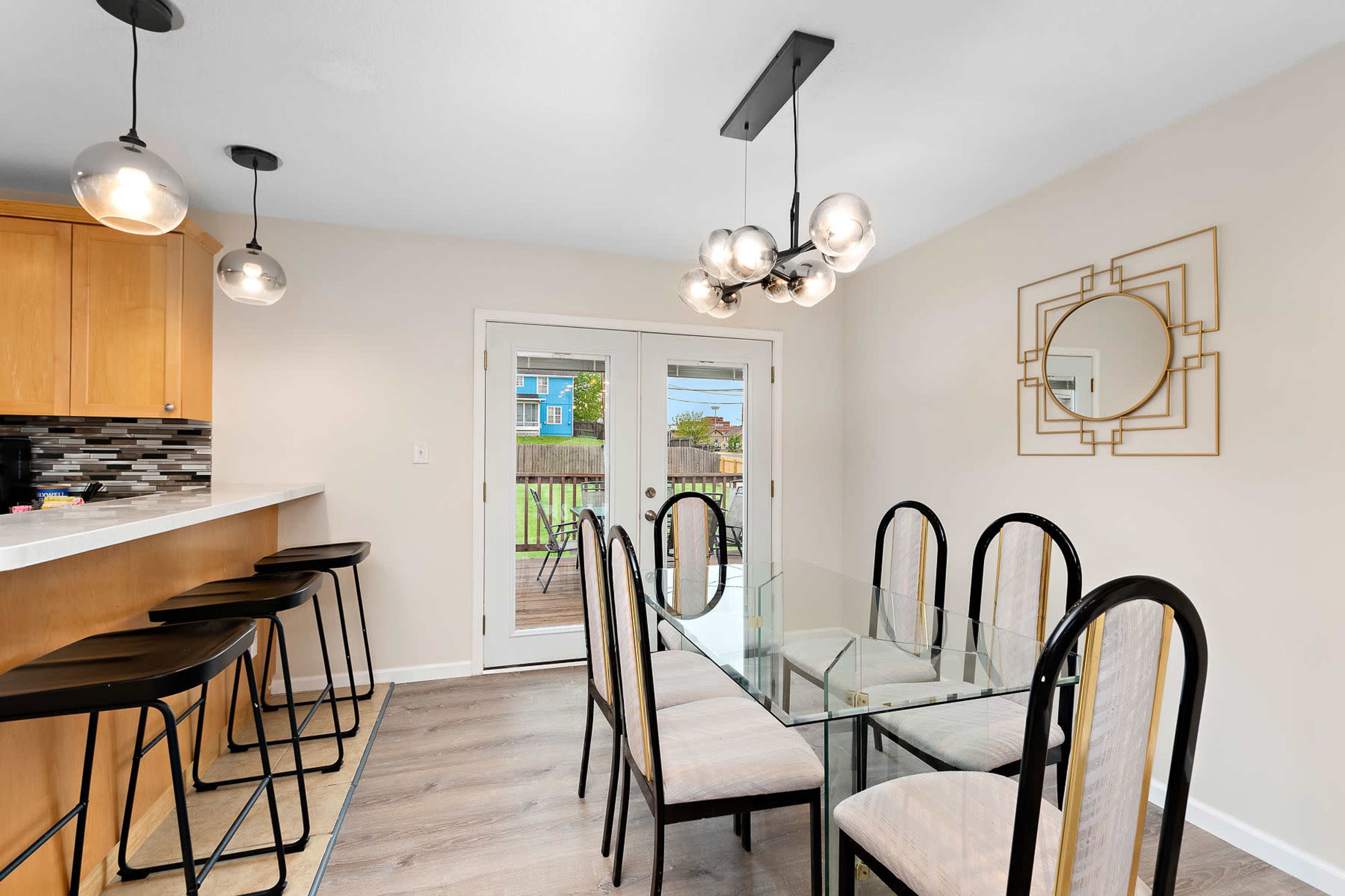A modern dining area features a glass table surrounded by black chairs, with a bar counter and pendant lights above.