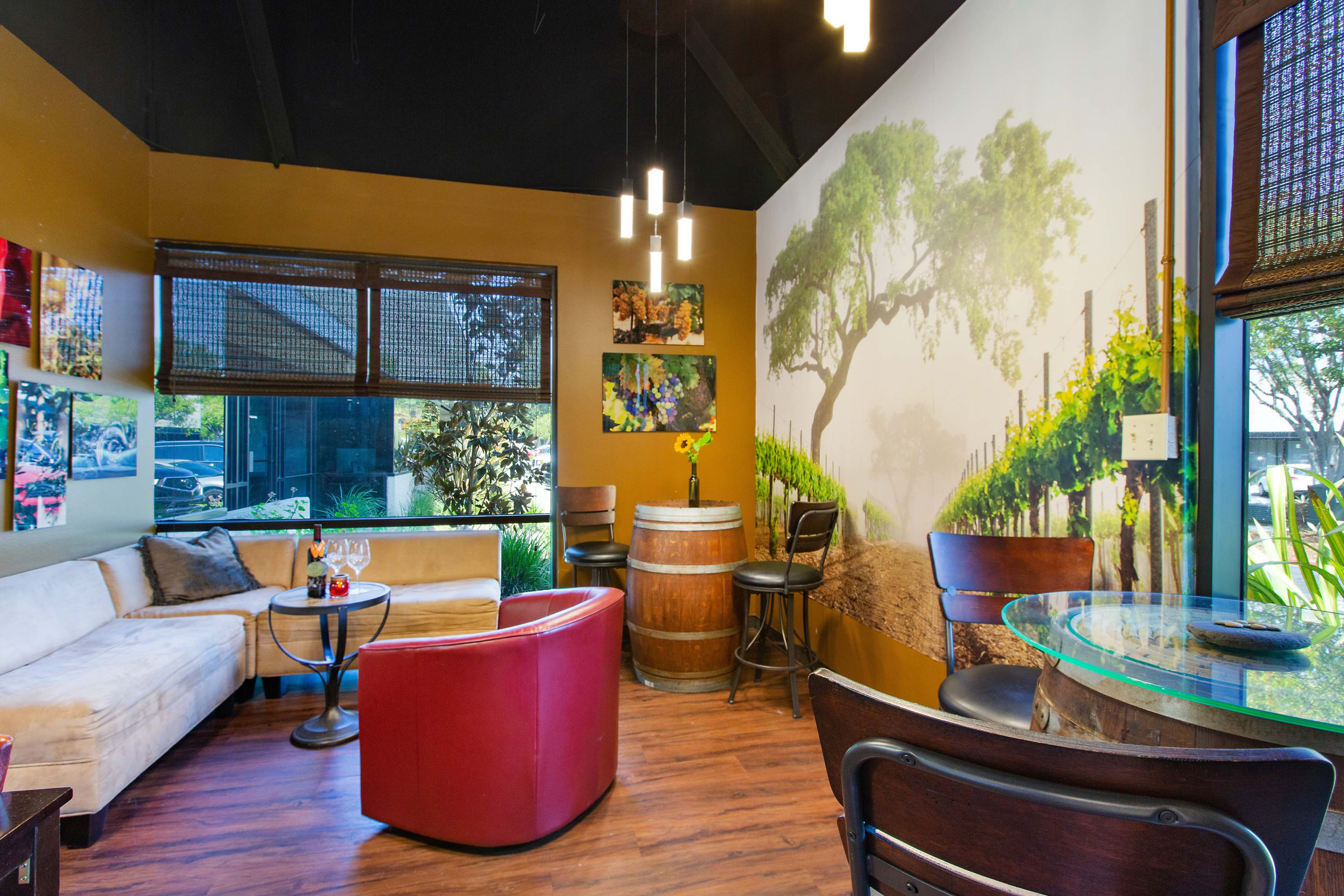 A cozy seating area with a curved couch, a round table, and a wine barrel against a mural of vineyard scenery on the wall.