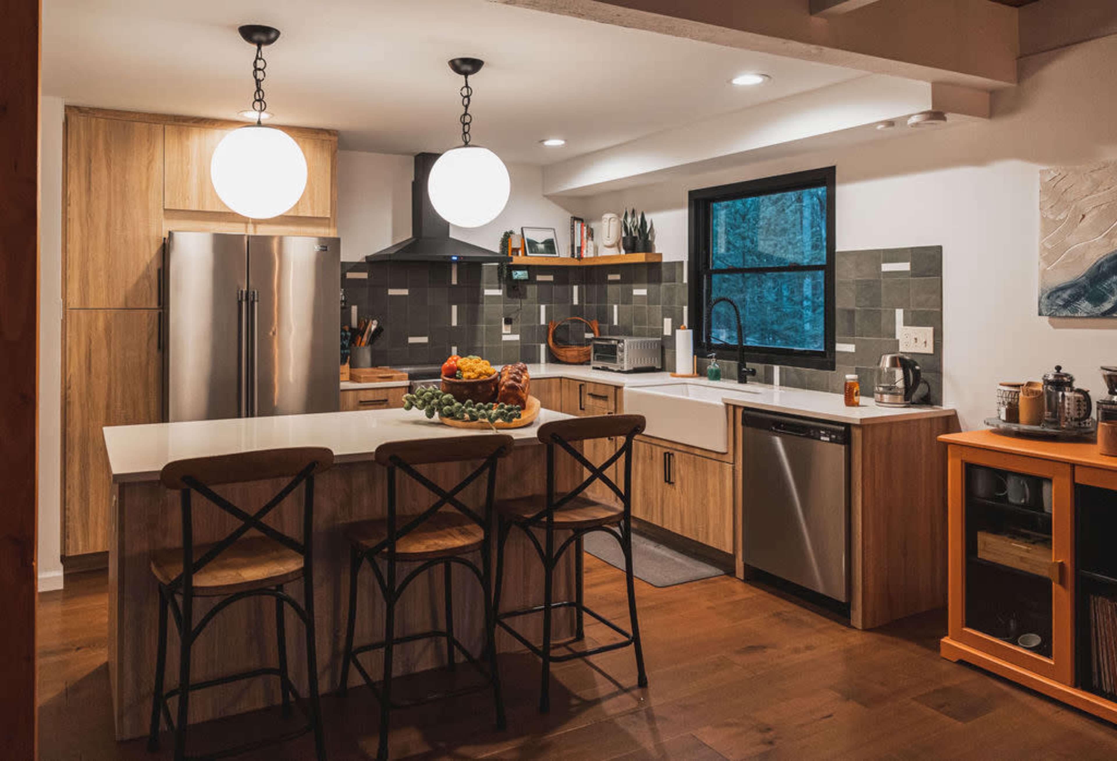 The image shows a modern kitchen with wooden cabinets, a large island with a fruit centerpiece, and stainless steel appliances.