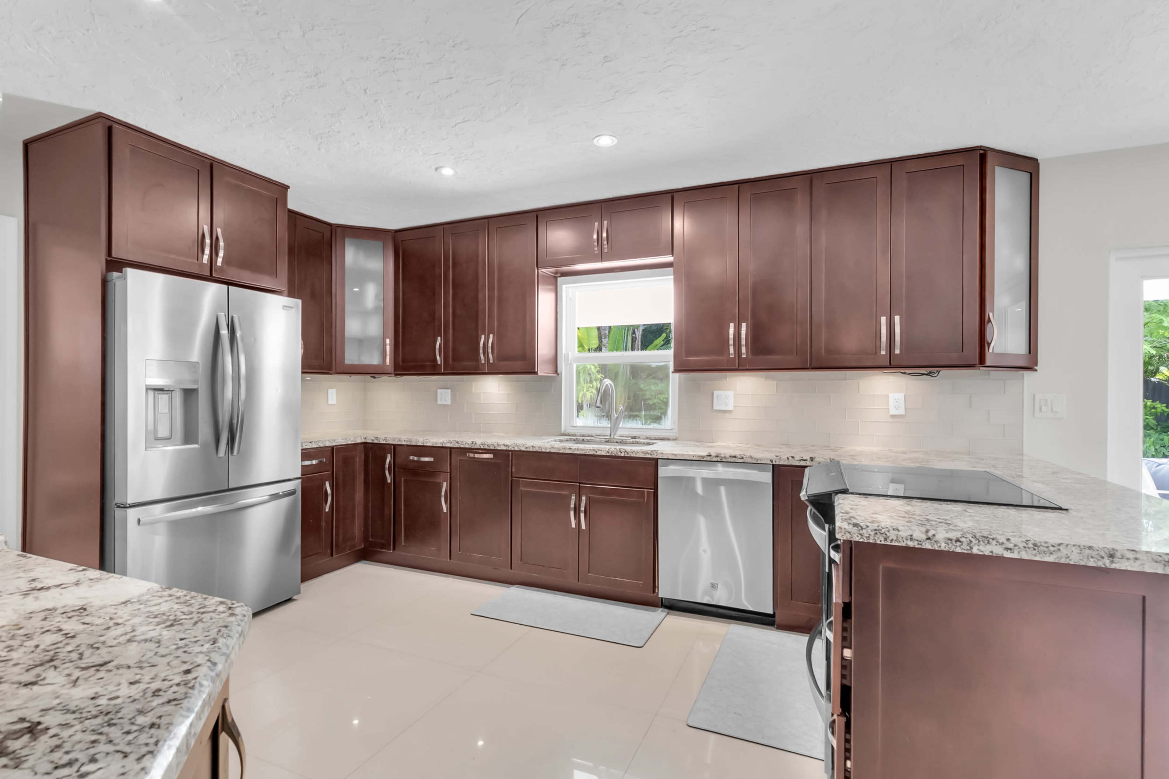 The image shows a modern kitchen featuring dark wood cabinets, a stainless steel refrigerator, and granite countertops with tile flooring.