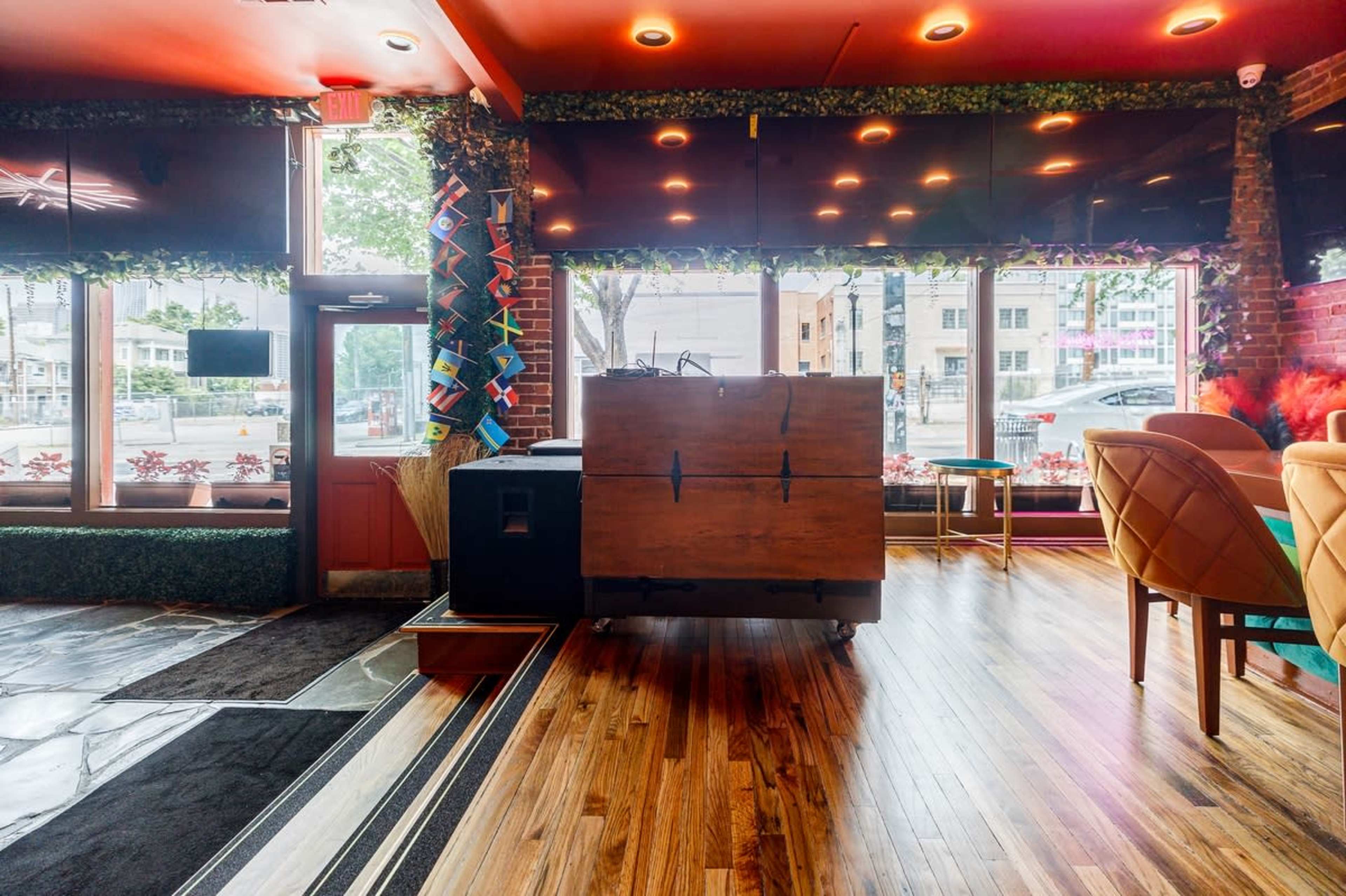 The interior of a restaurant with wooden flooring, a large wooden counter, and plants lining the windows.