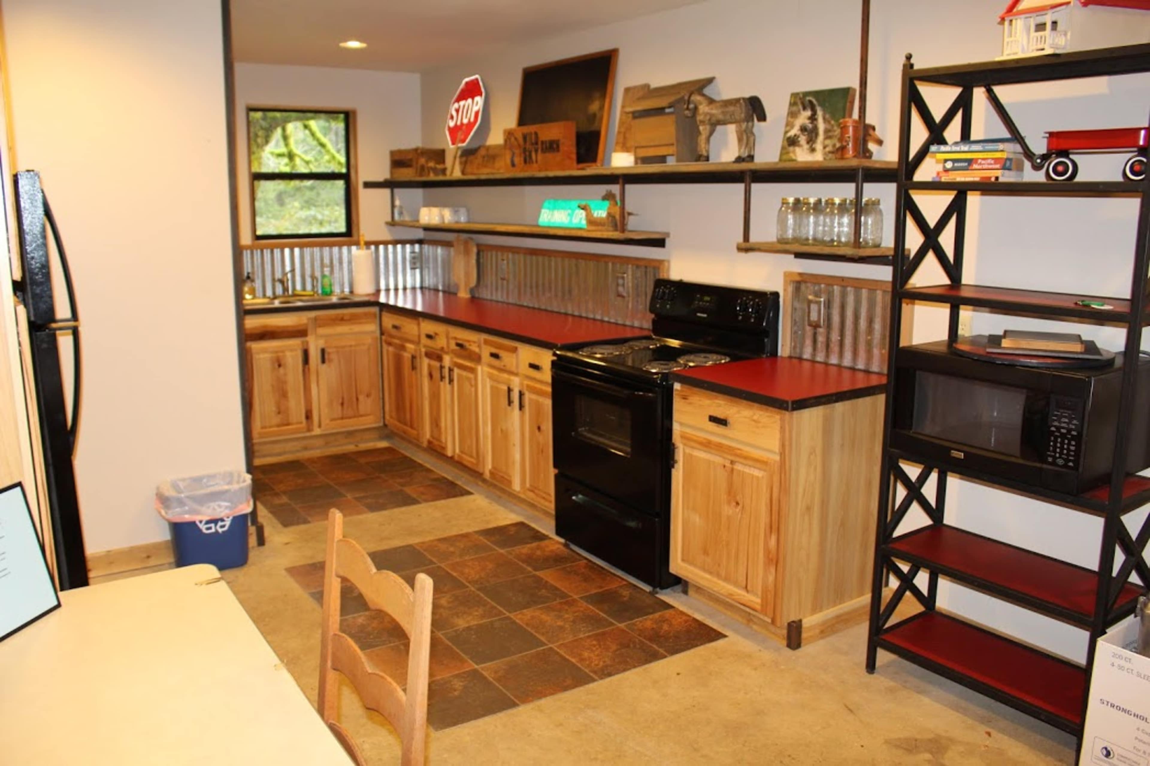 A kitchen with wooden cabinets, a black stove, a microwave, and open shelving, featuring a tiled floor and a small table with chairs.