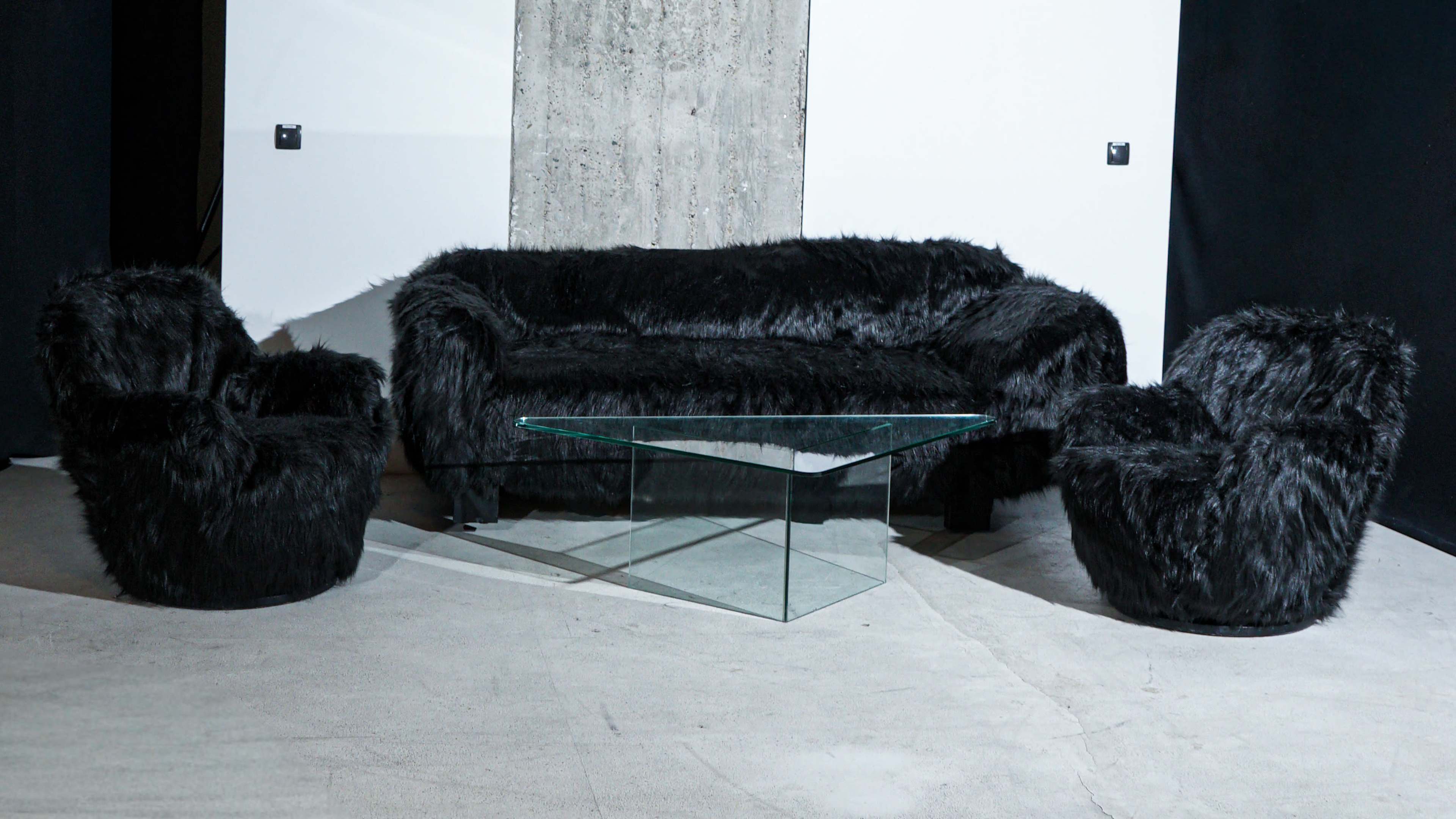 The image shows a modern living room setup featuring a black furry sofa and two matching armchairs around a glass coffee table.