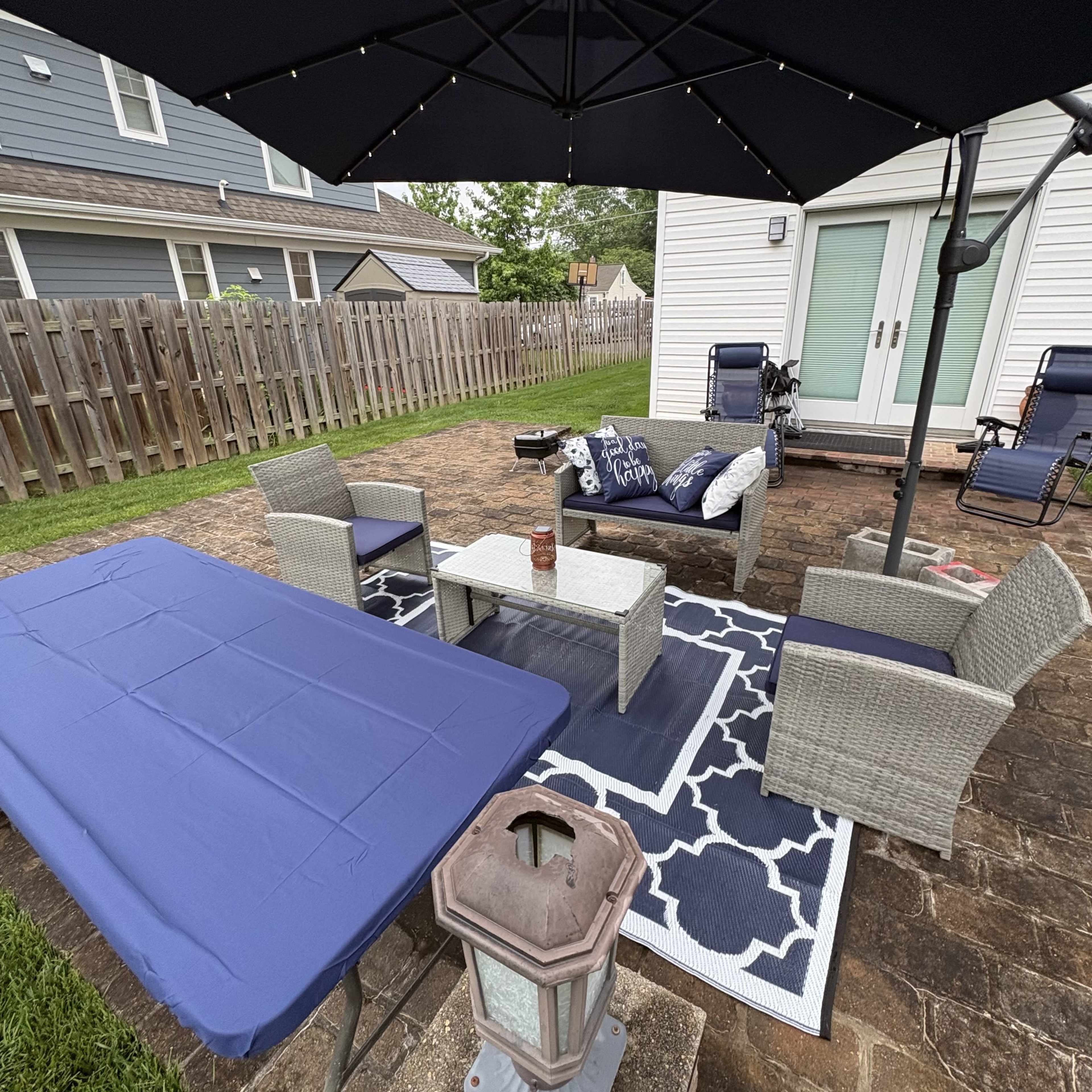 The image shows a patio area with a seating arrangement, including a couch and chairs under an umbrella, along with a table and a decorative rug.