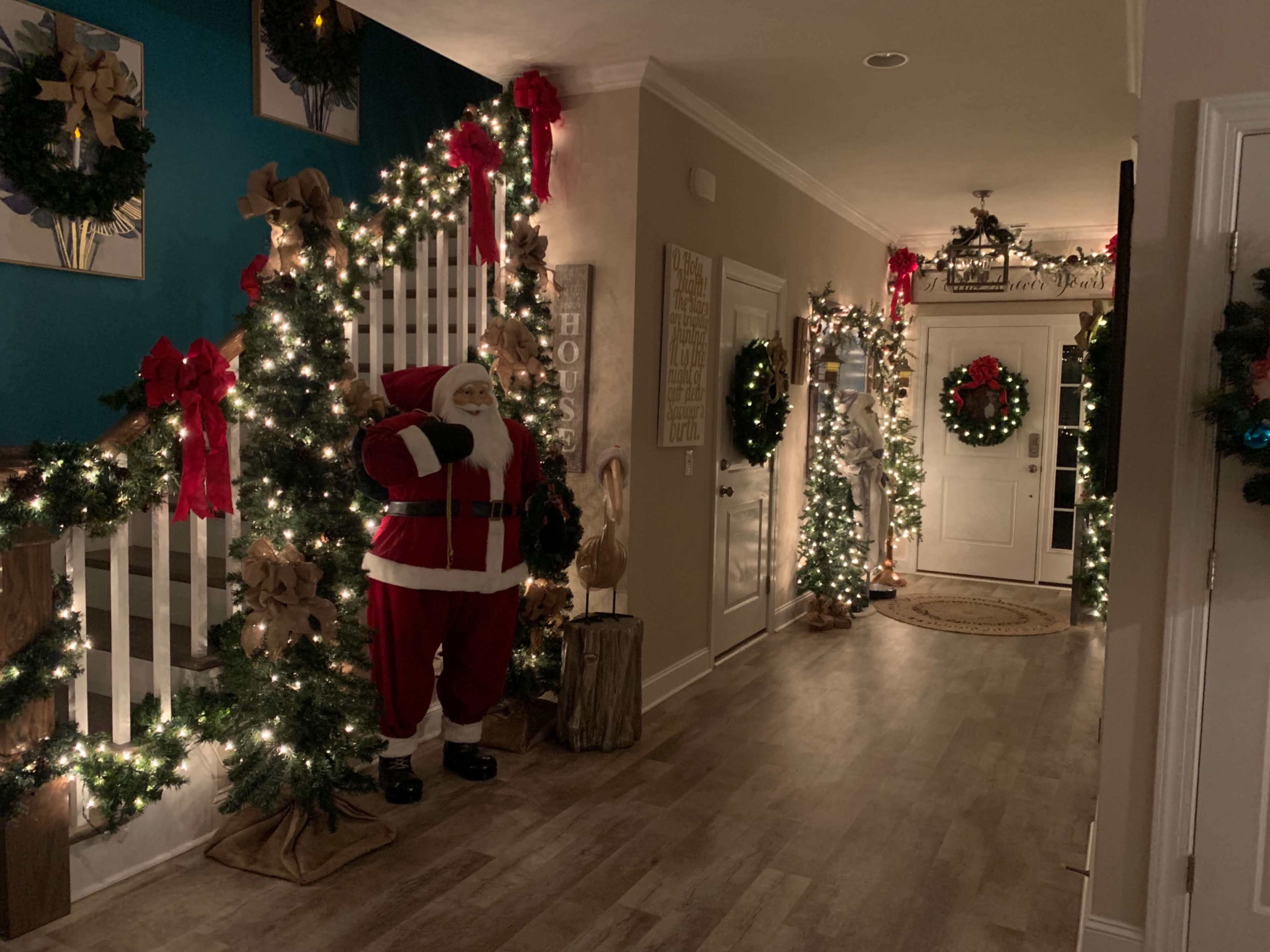 The hallway is decorated for the holidays with Christmas trees, wreaths, and lights, featuring a Santa Claus figure near the staircase.