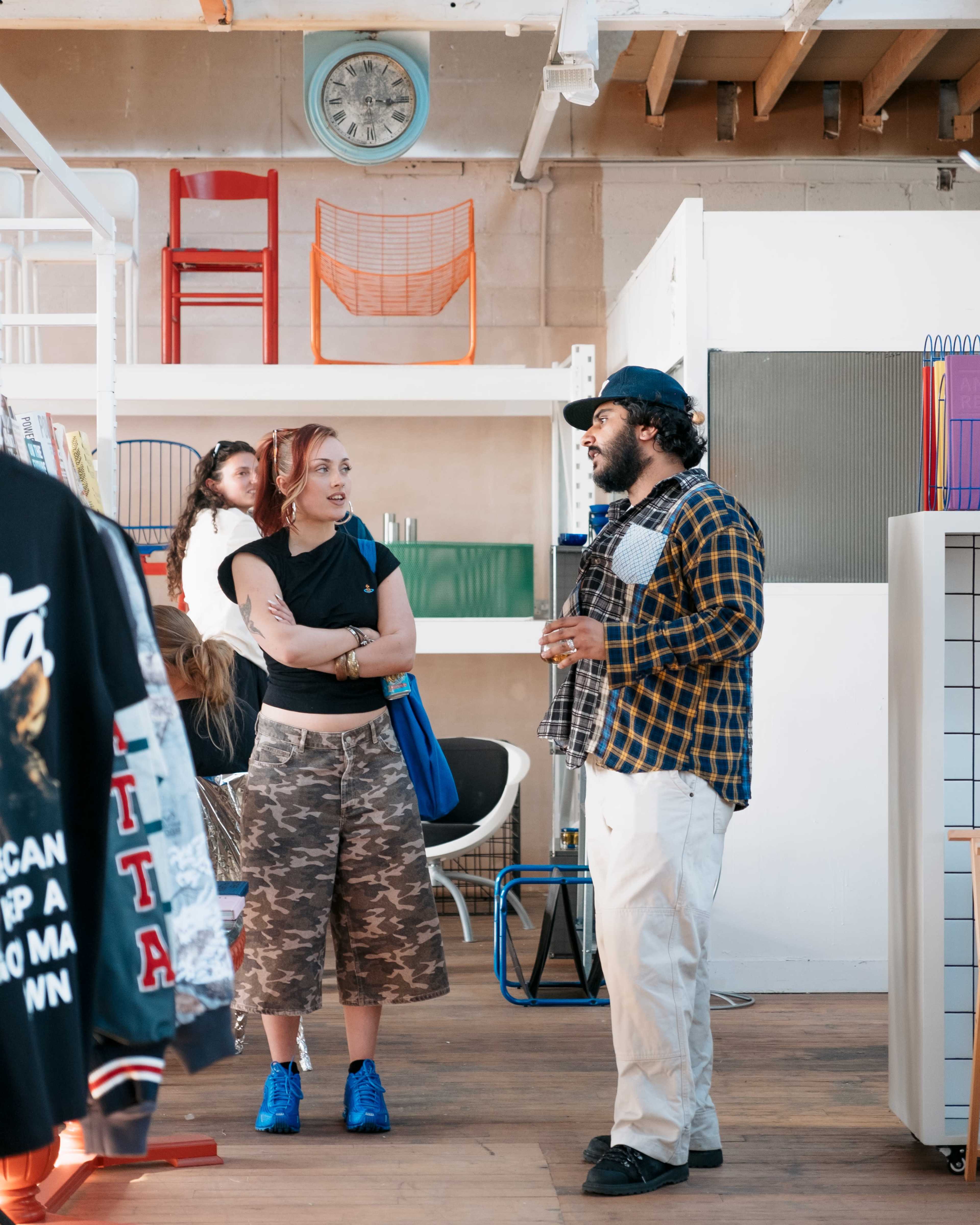 Two people are conversing in a stylish retail space filled with clothing and colorful furniture.