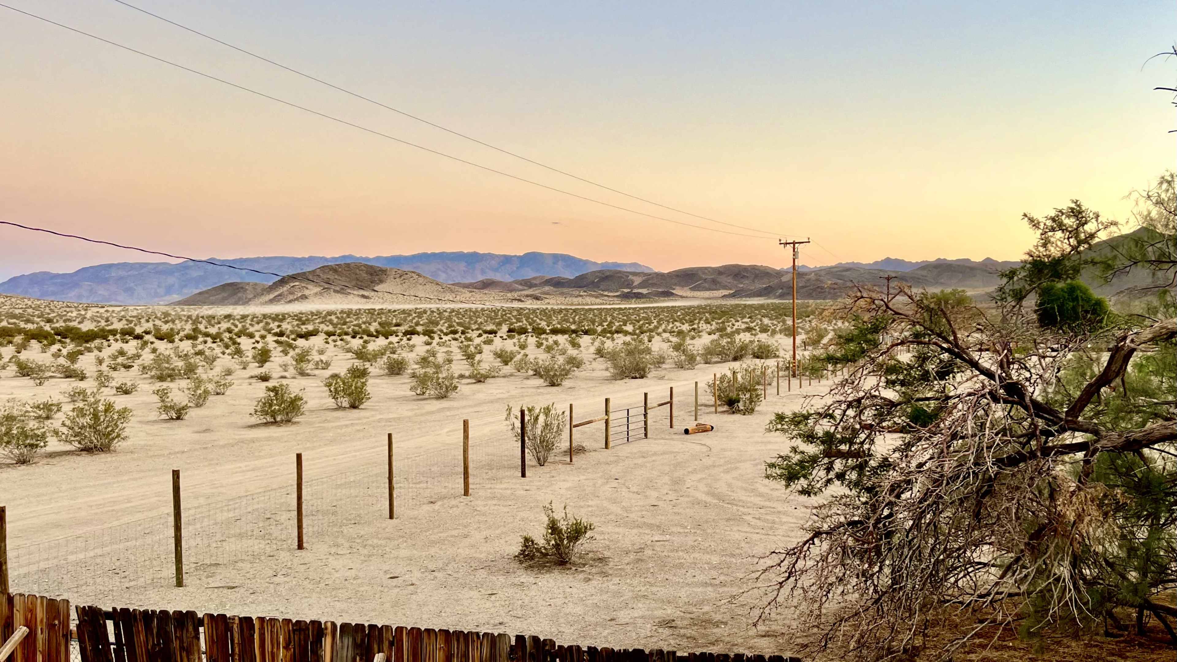 The scene shows a sparsely vegetated desert landscape with distant mountains under a fading sunset.