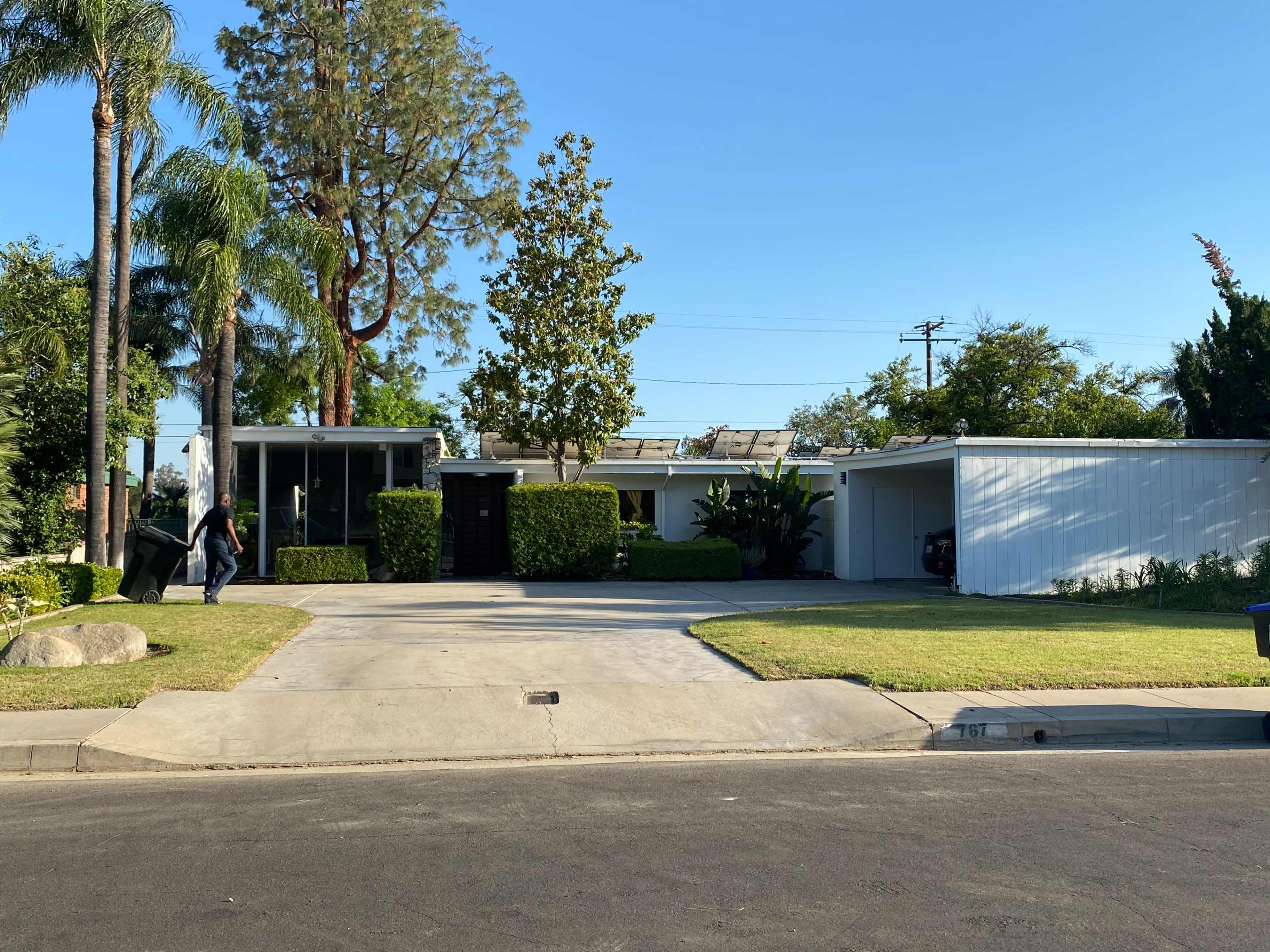 A modern single-story house with a glass front, landscaped yard, and a driveway leading to a garage.