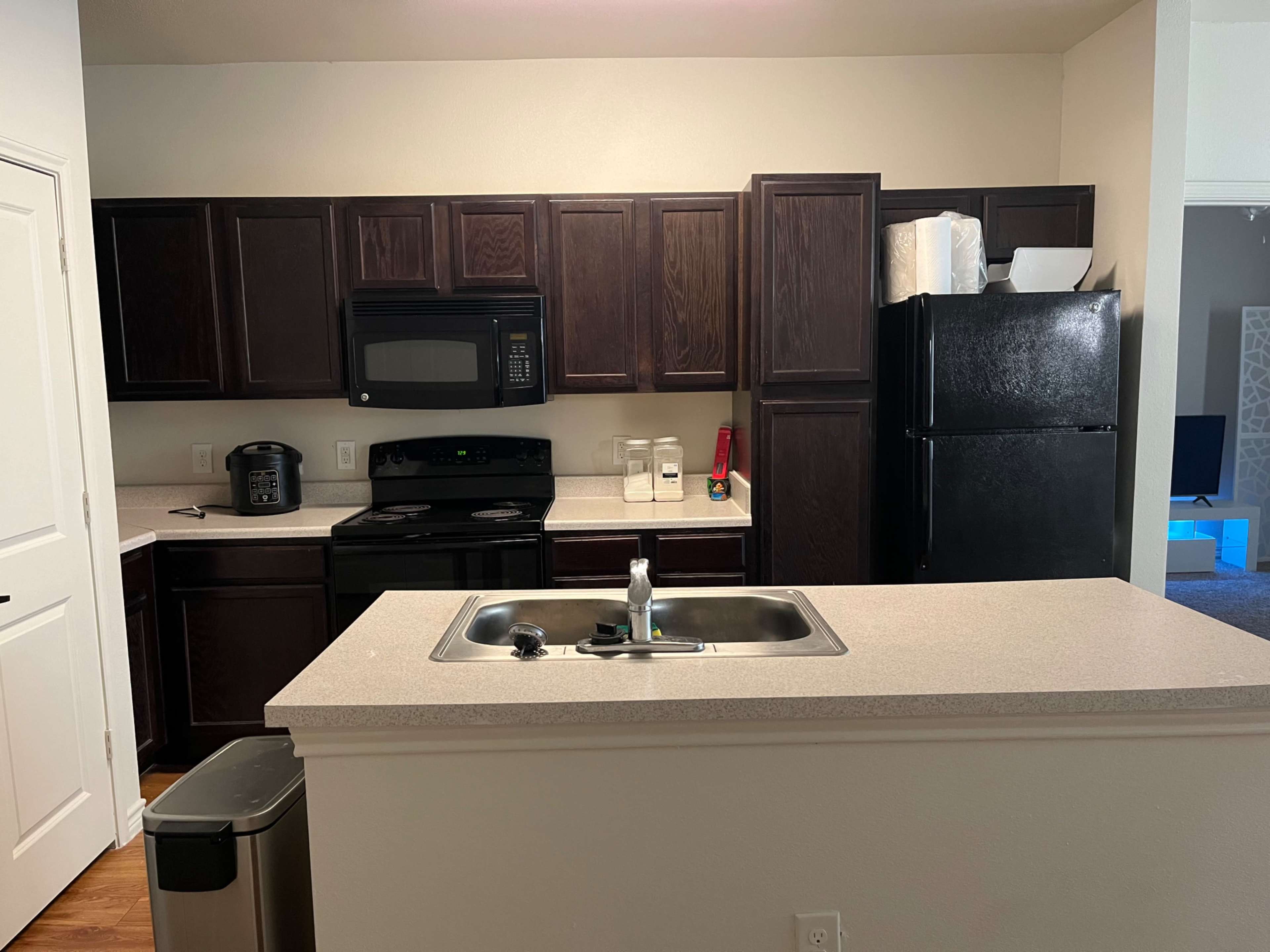 A modern kitchen with dark wood cabinets, a black refrigerator, an oven, and a countertop with a sink.