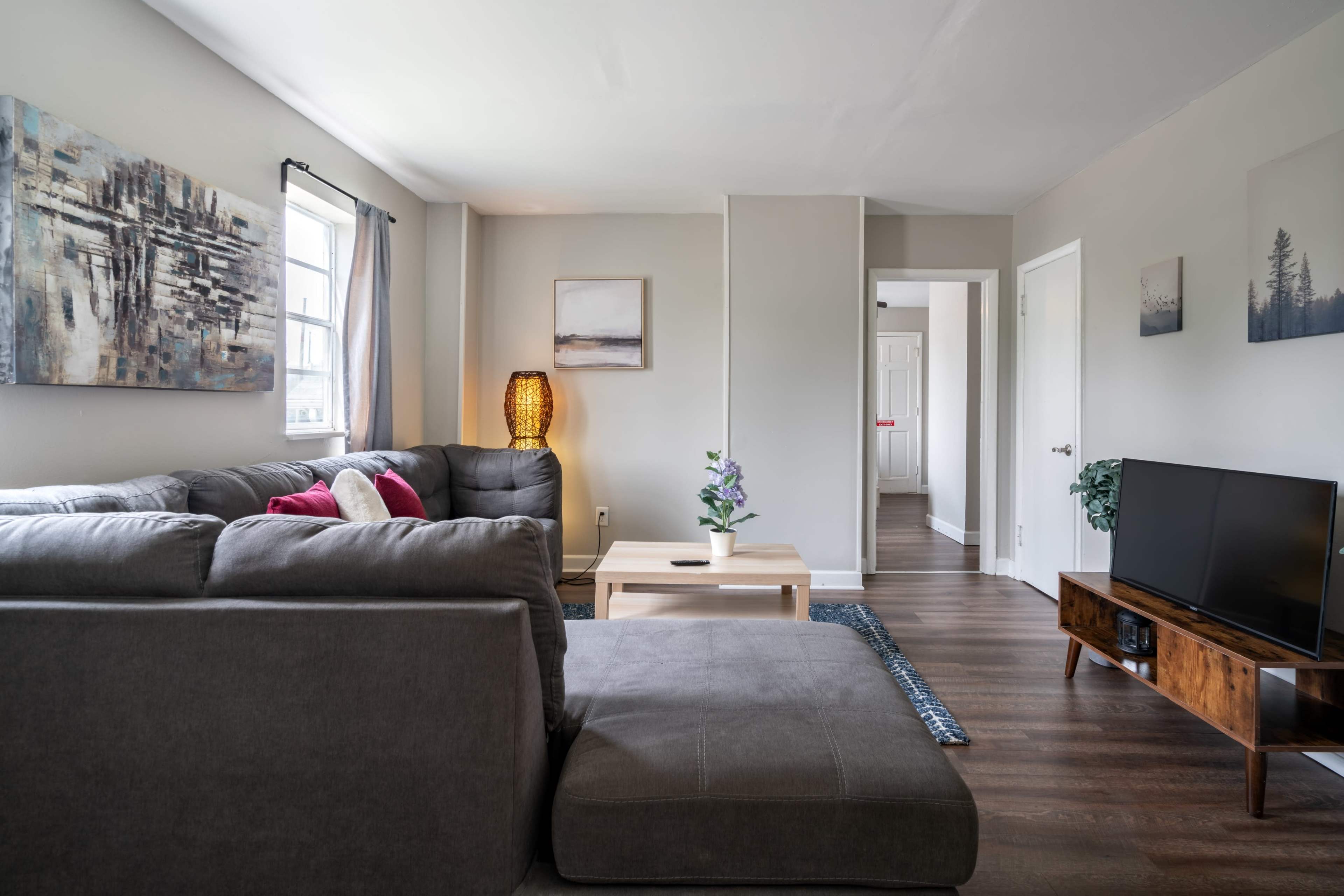 The image shows a modern living room with a gray sectional sofa, a coffee table, a television, and artwork on the walls.