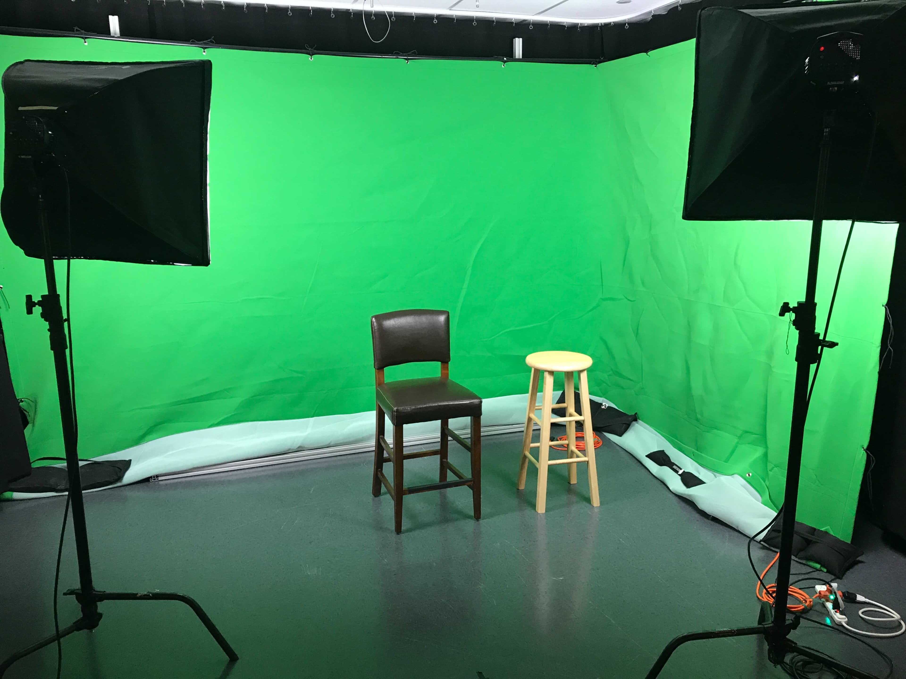 A studio setup with a green screen backdrop, featuring a brown wooden chair and a yellow stool positioned in front of it.