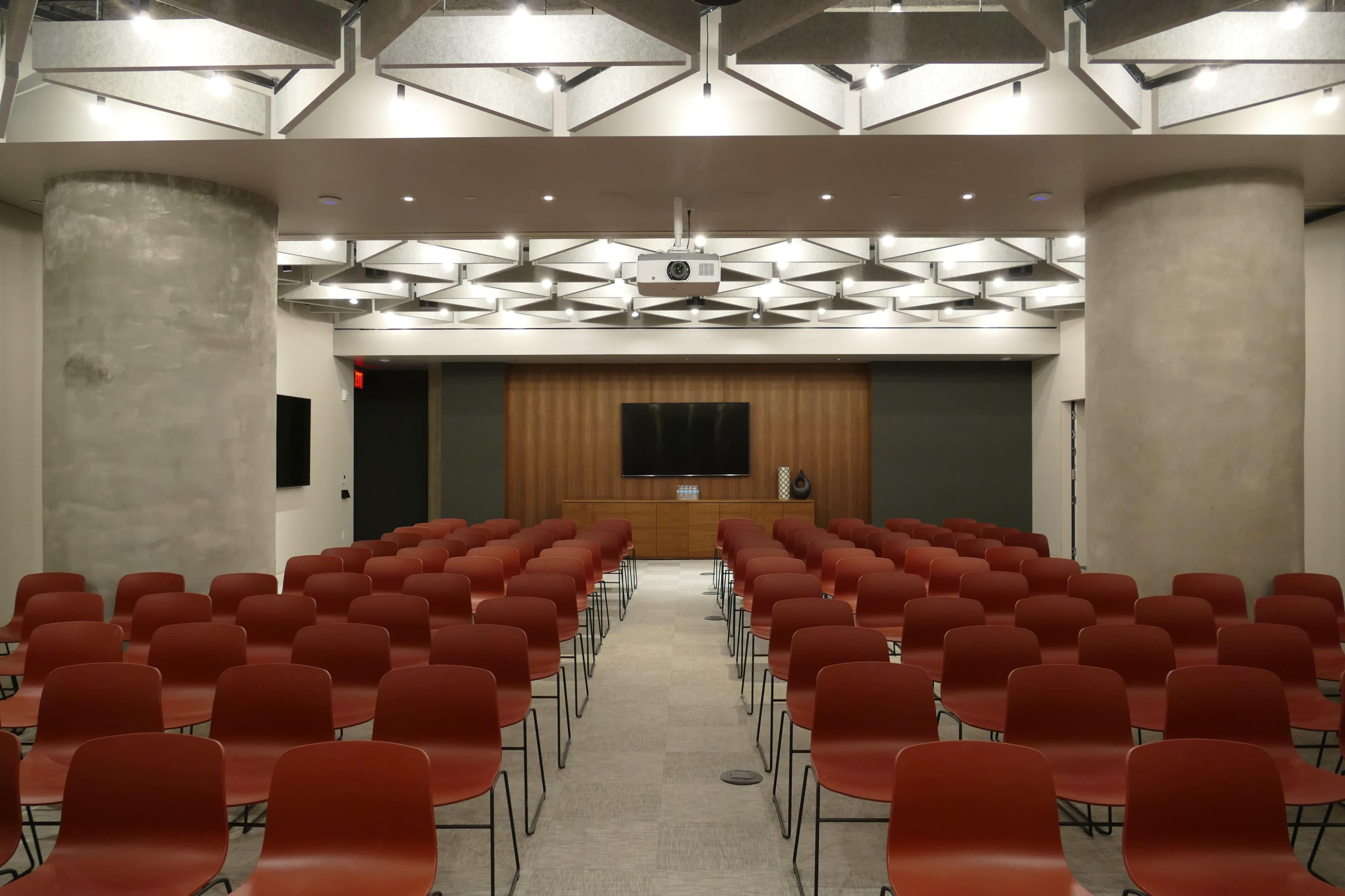 A conference room set up with rows of red chairs facing a wooden wall with a television and projector.