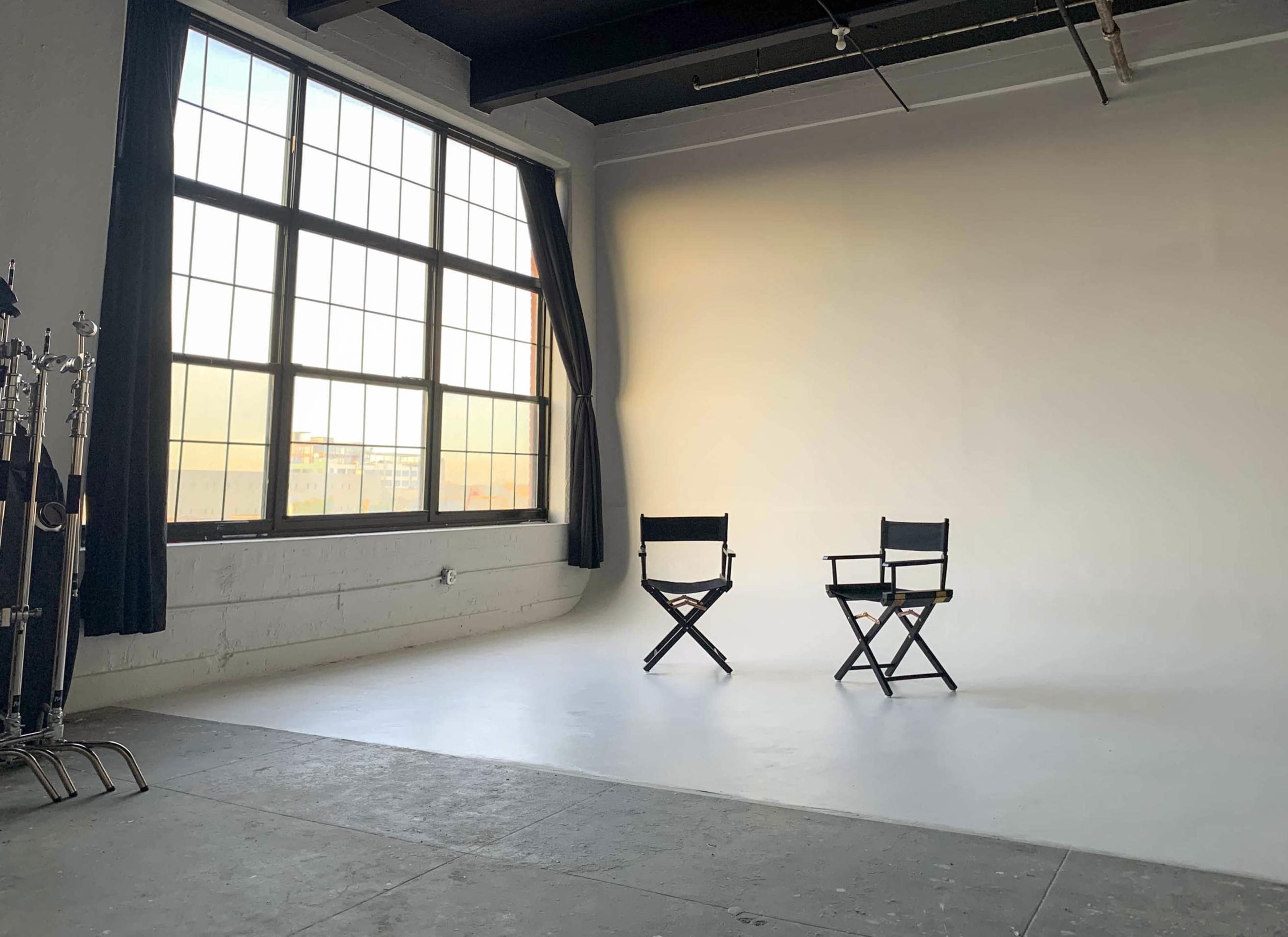 A well-lit studio space featuring two director's chairs facing each other in front of a large window.