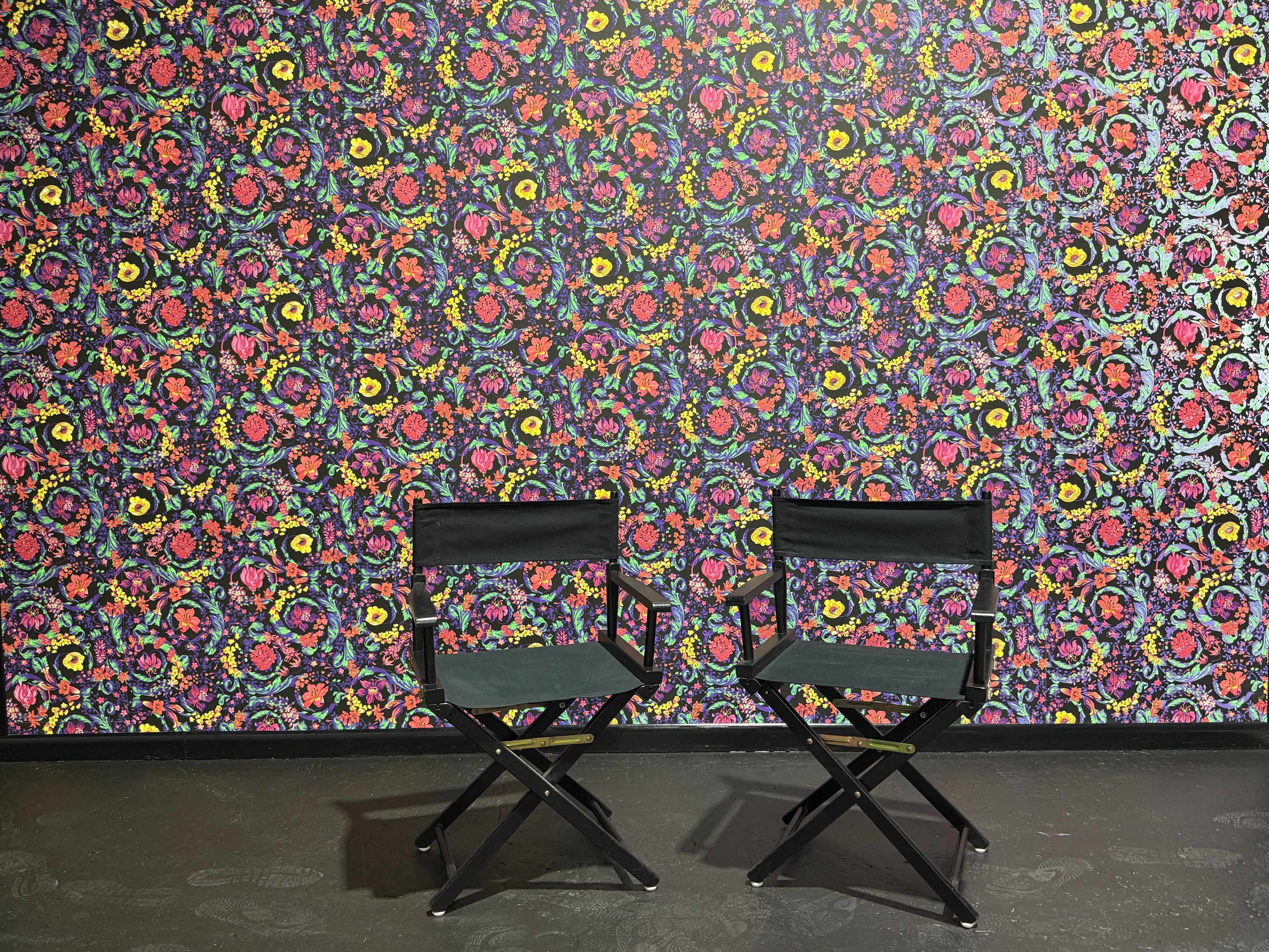 Two black director's chairs are positioned in front of a vibrant floral-patterned wall.