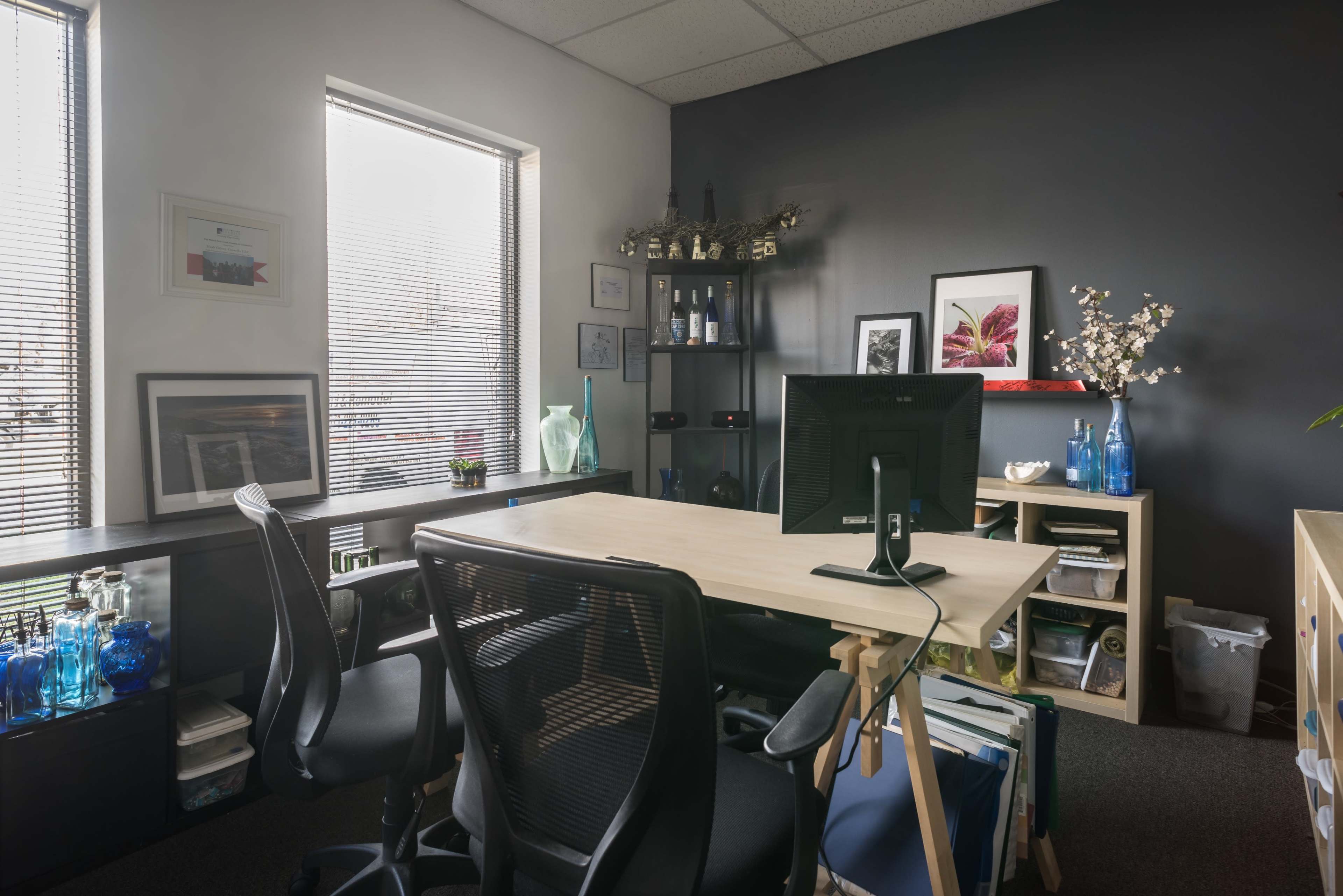 A modern office space features a desk with a computer, dual chairs, decorative plants, and organized shelves along the walls.