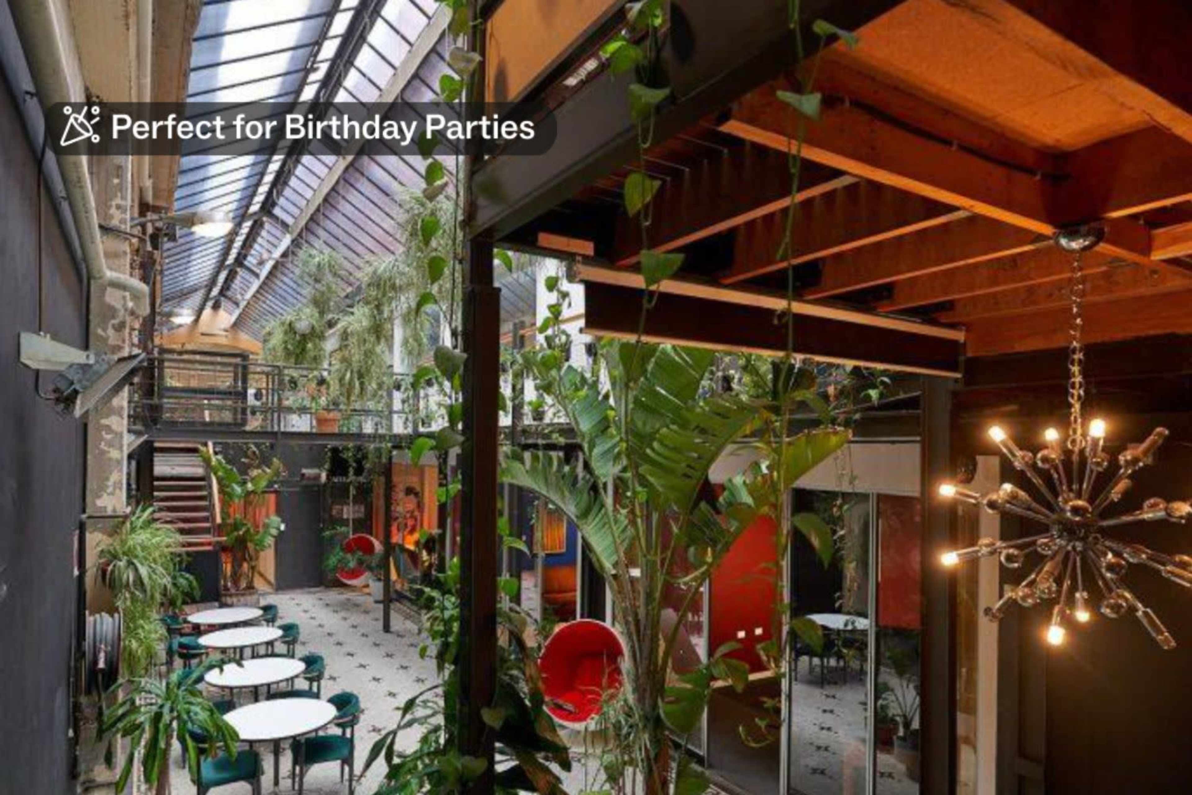 A brightly lit indoor space filled with greenery, featuring dining tables and chairs arranged throughout.