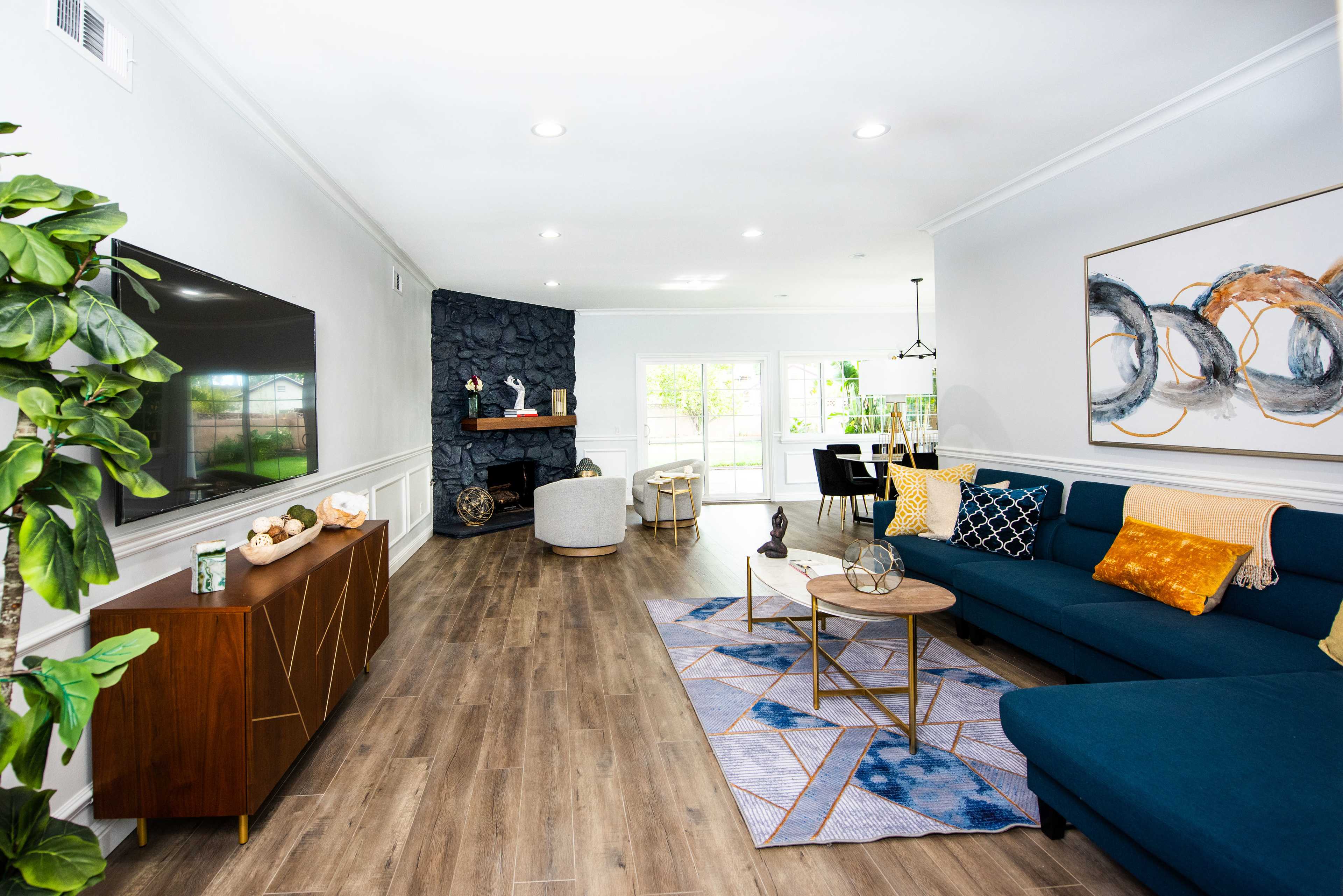 A modern living room featuring a blue sectional sofa, a wooden coffee table, a stone fireplace, and large windows that bring in natural light.