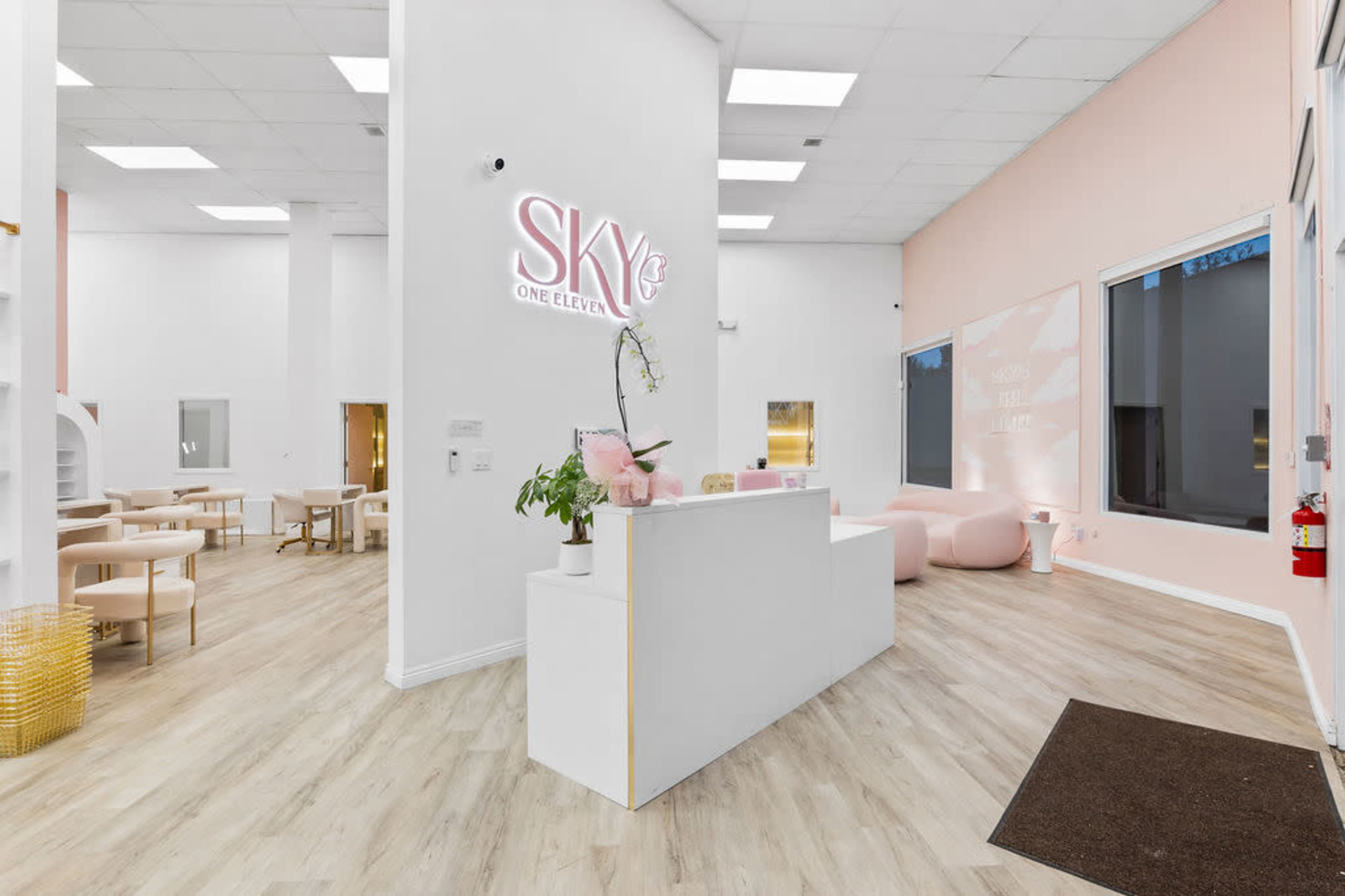 A modern reception area with a white desk, light-colored flooring, and pink walls featuring large windows.