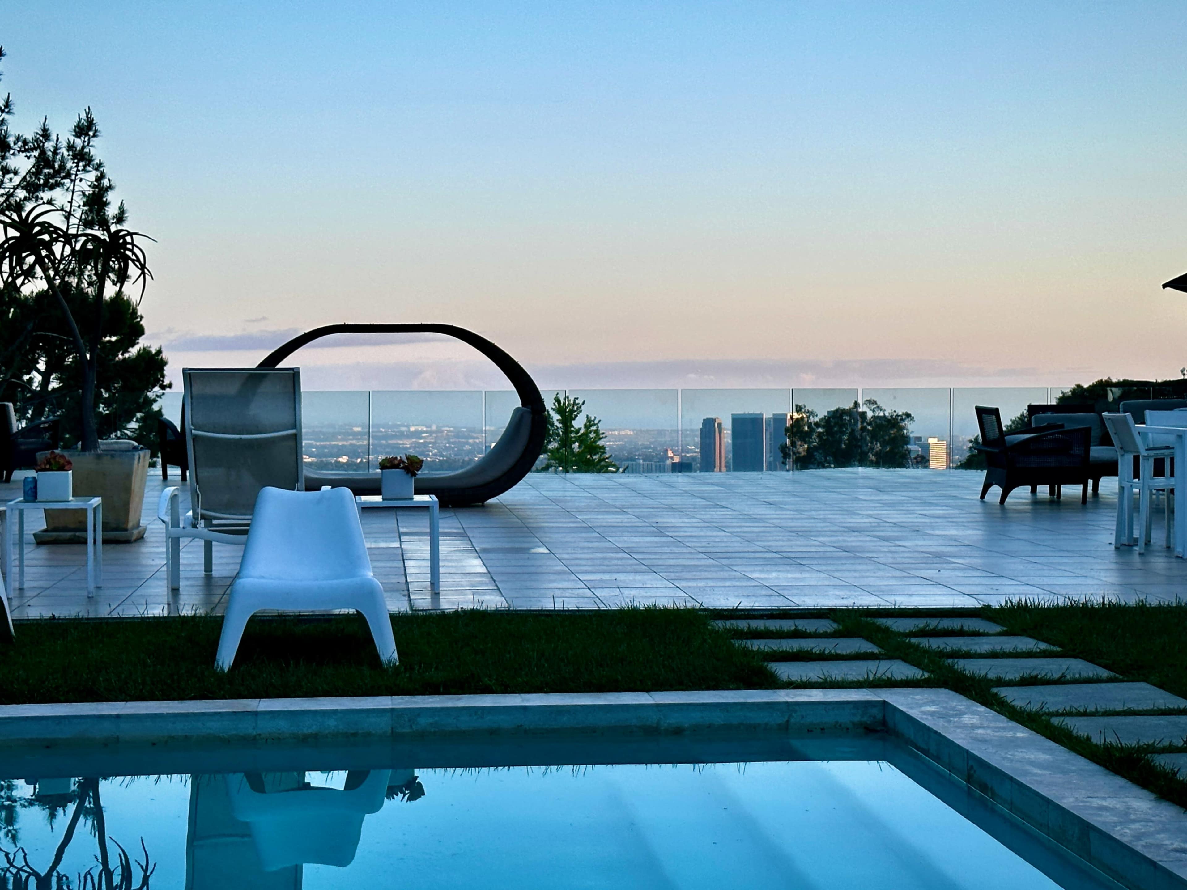 A terrace with modern outdoor furniture overlooking a city skyline and a swimming pool in the foreground.