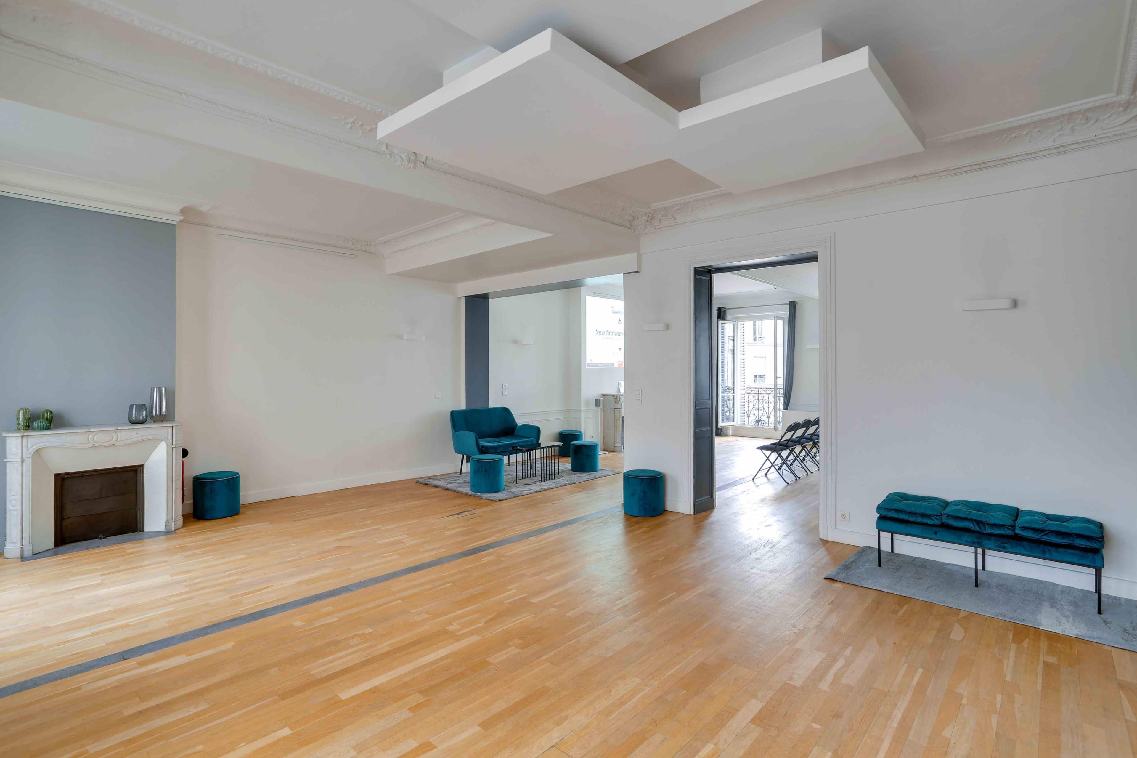 The image shows a spacious, minimally furnished room with light hardwood flooring, a blue couch, and two seating areas separated by a partition.