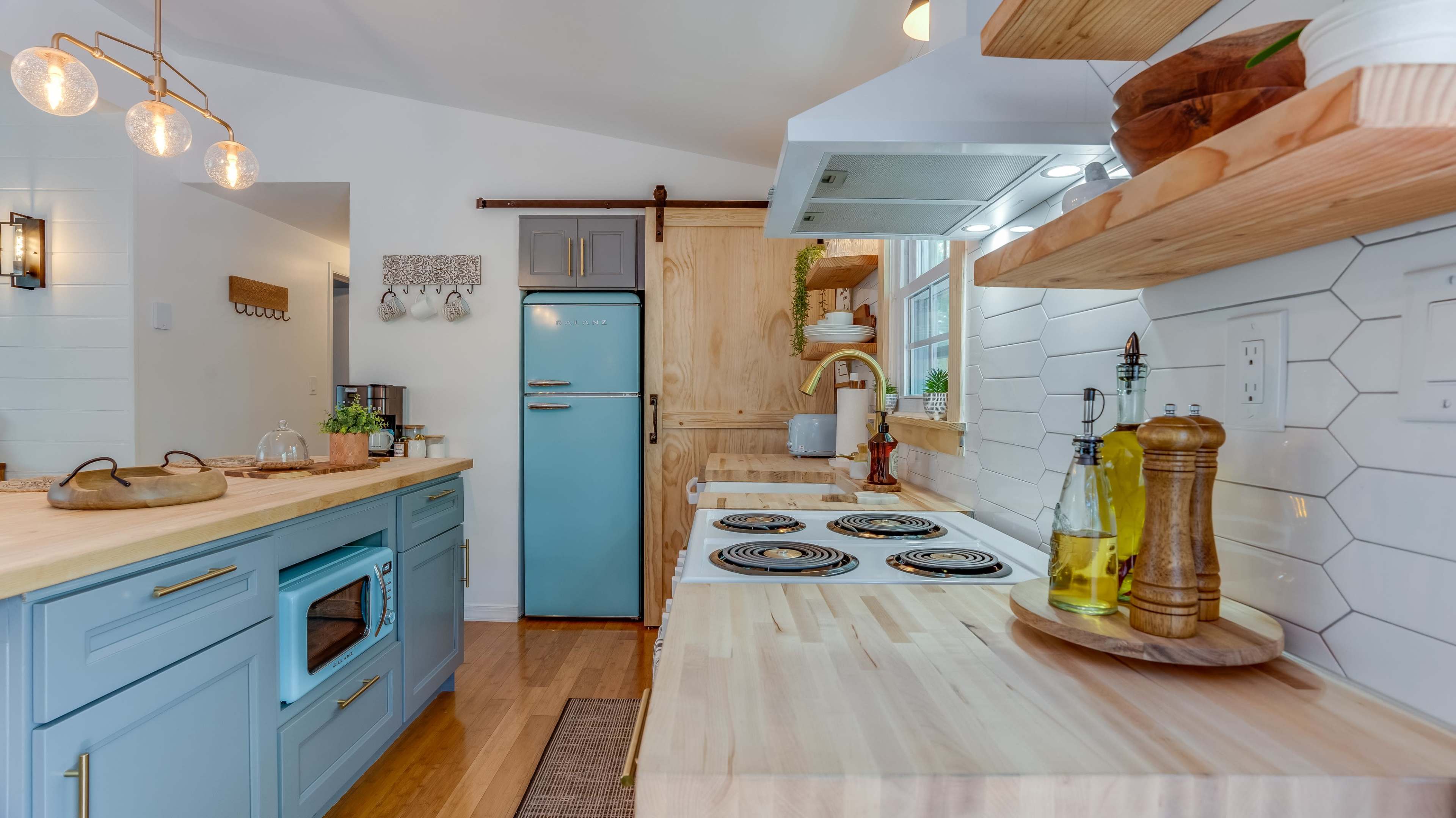 The image shows a modern kitchen with light blue cabinetry, a sliding barn door, and wooden shelves displaying kitchen items.