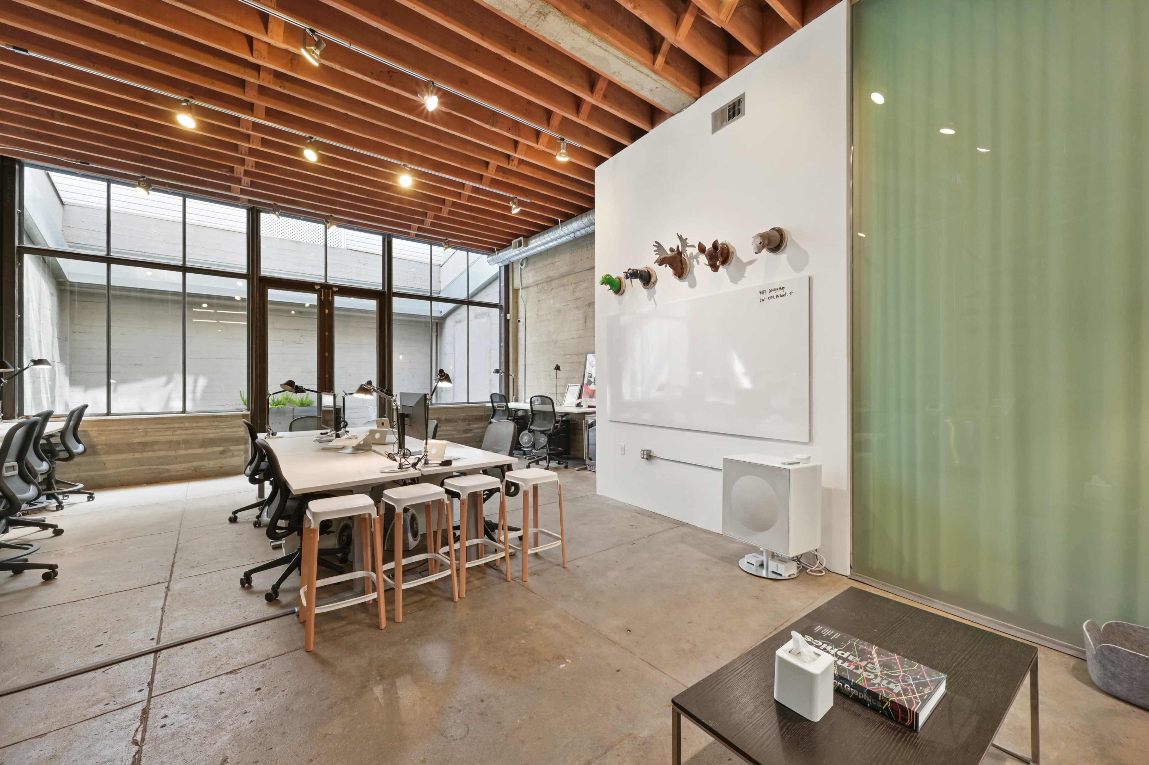 A spacious office features wooden beams, multiple workstations with computers, and a white wall adorned with decorative elements.