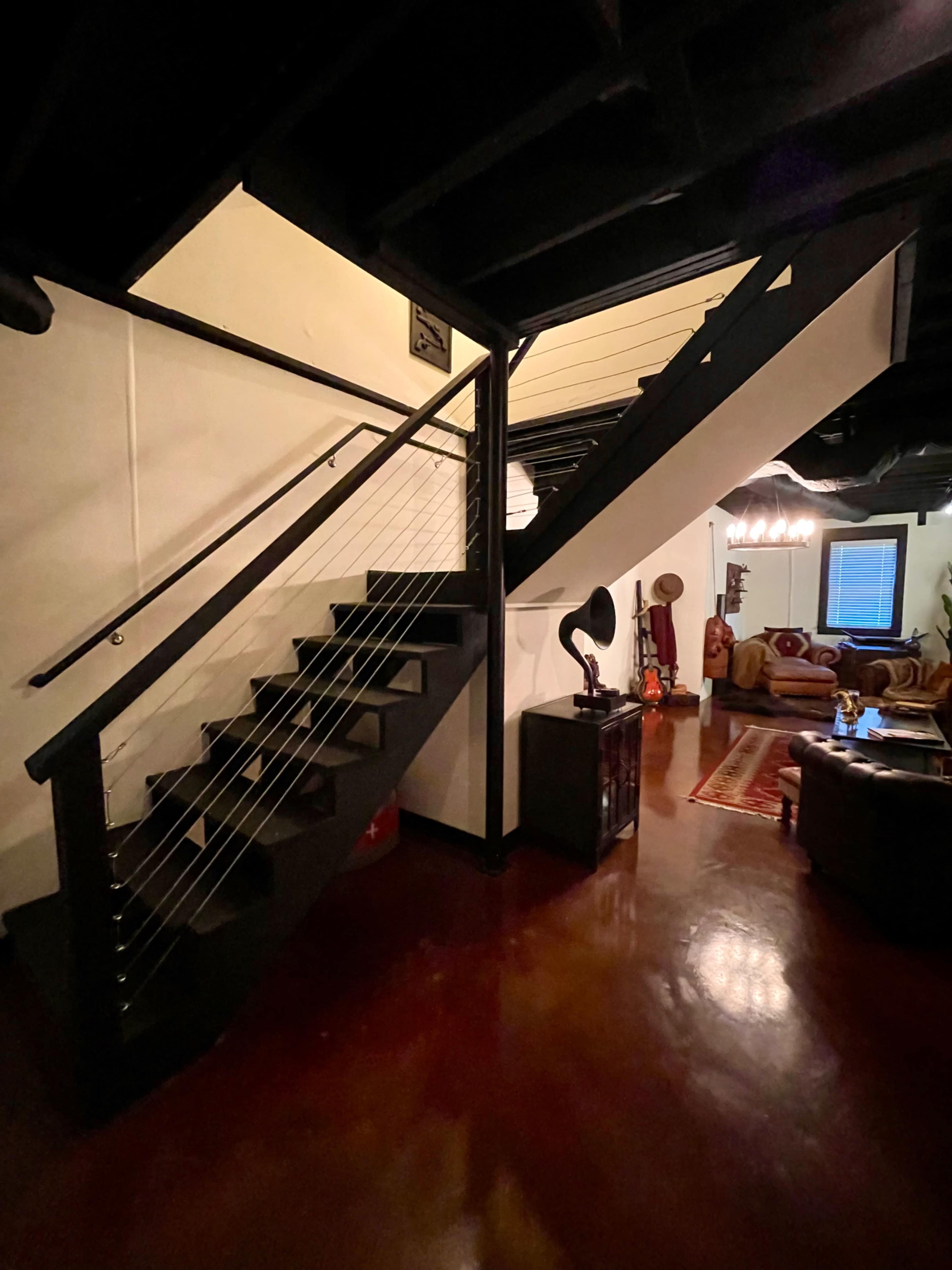 A well-lit staircase with a black railing leading to an upper level, adjacent to a cozy living area with vintage decor.