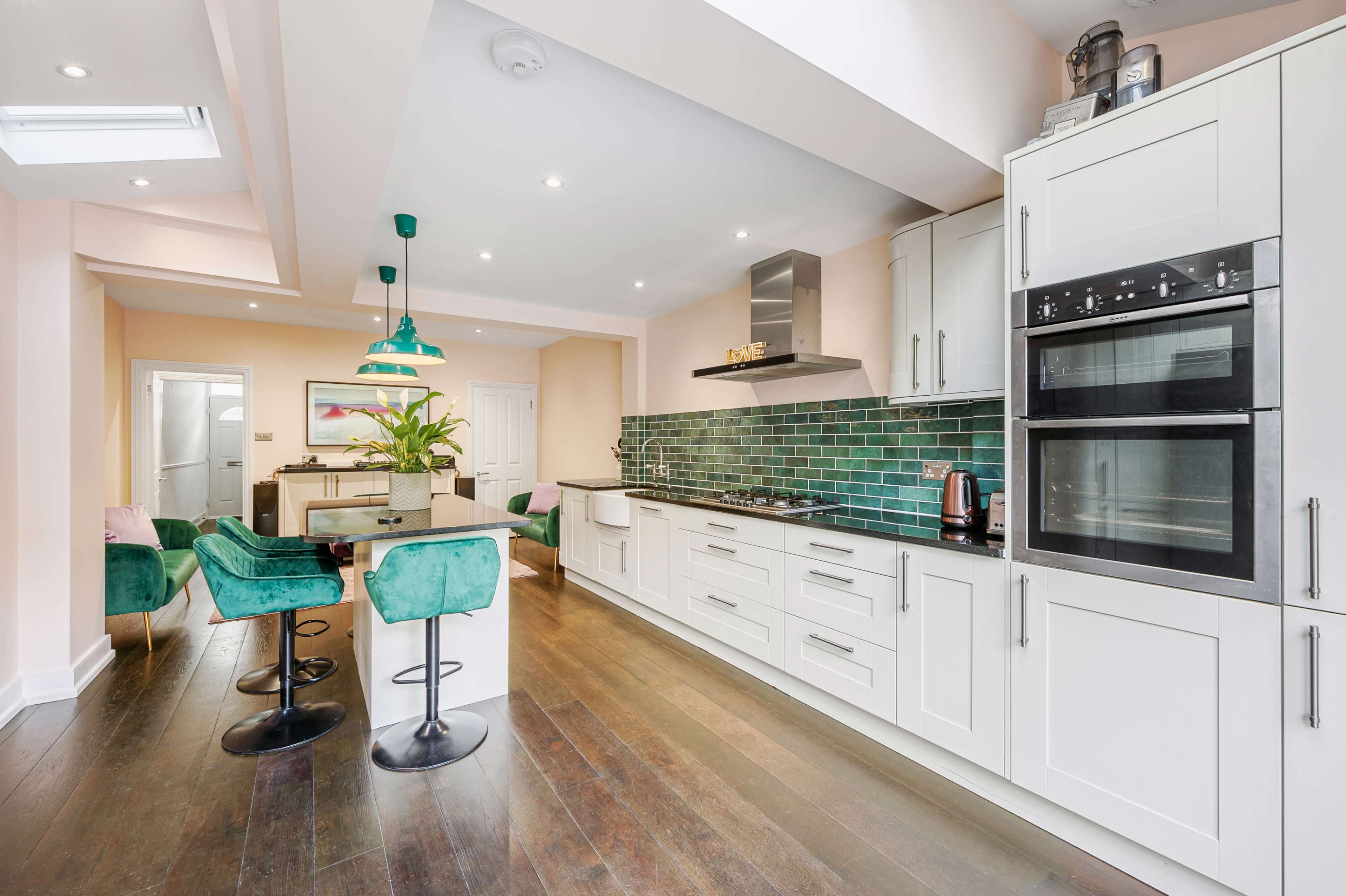 A modern kitchen with a tiled backsplash, an island with green upholstered chairs, and built-in appliances.