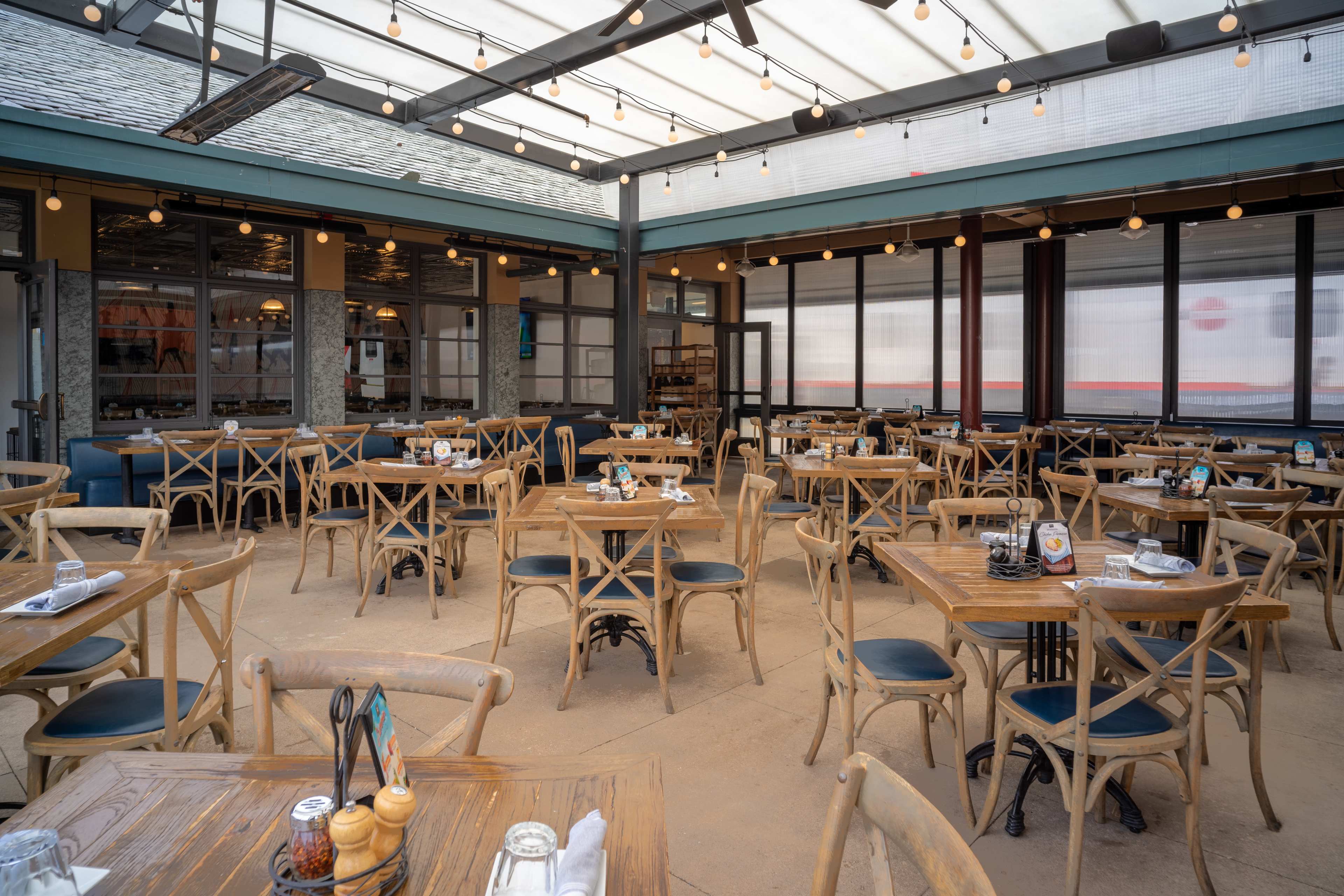 The image shows an indoor dining area with wooden tables and chairs arranged neatly, illuminated by overhead string lights.