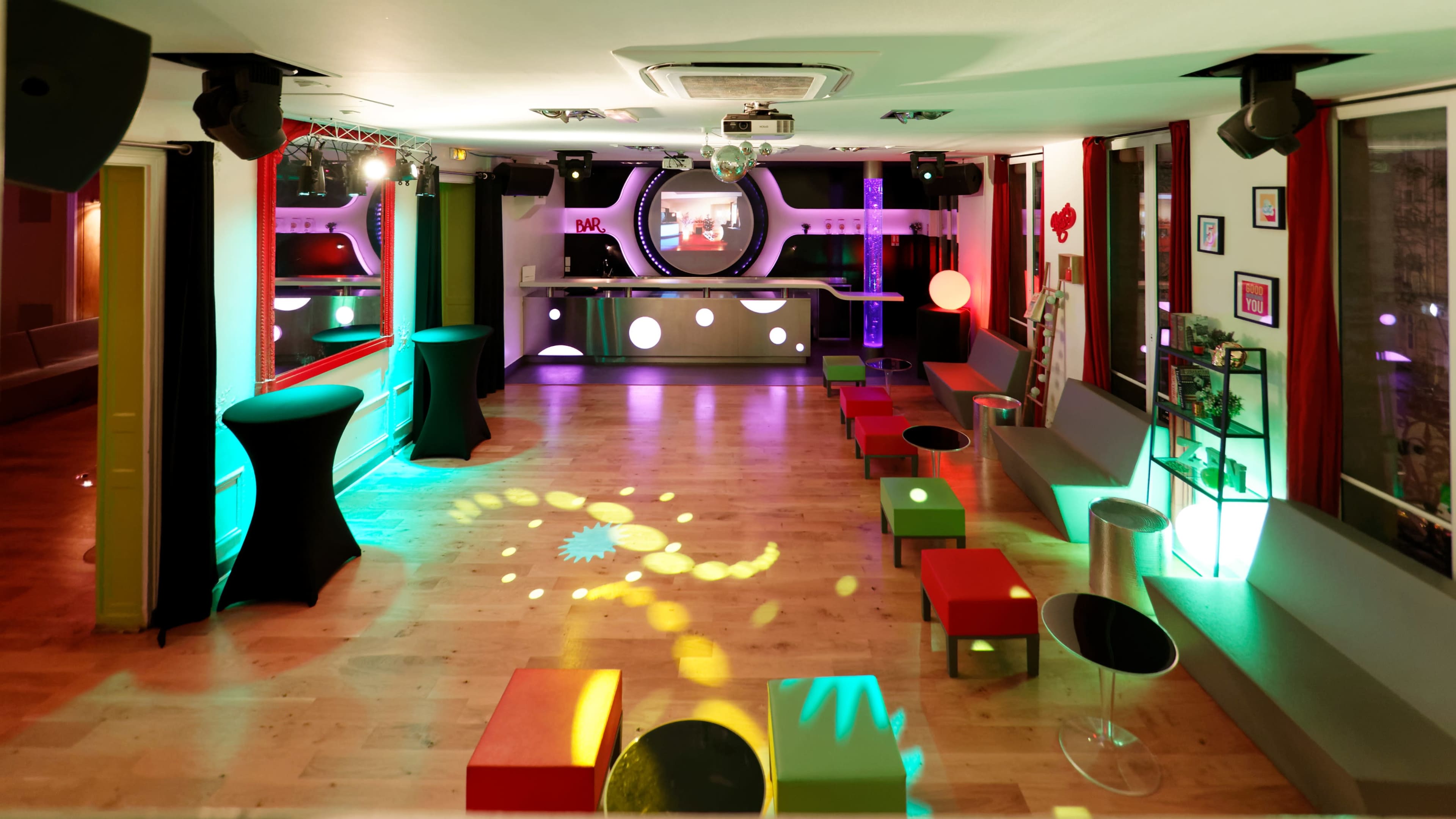 A brightly lit lounge area features colorful furniture and a bar in the background, designed for social gatherings and events.