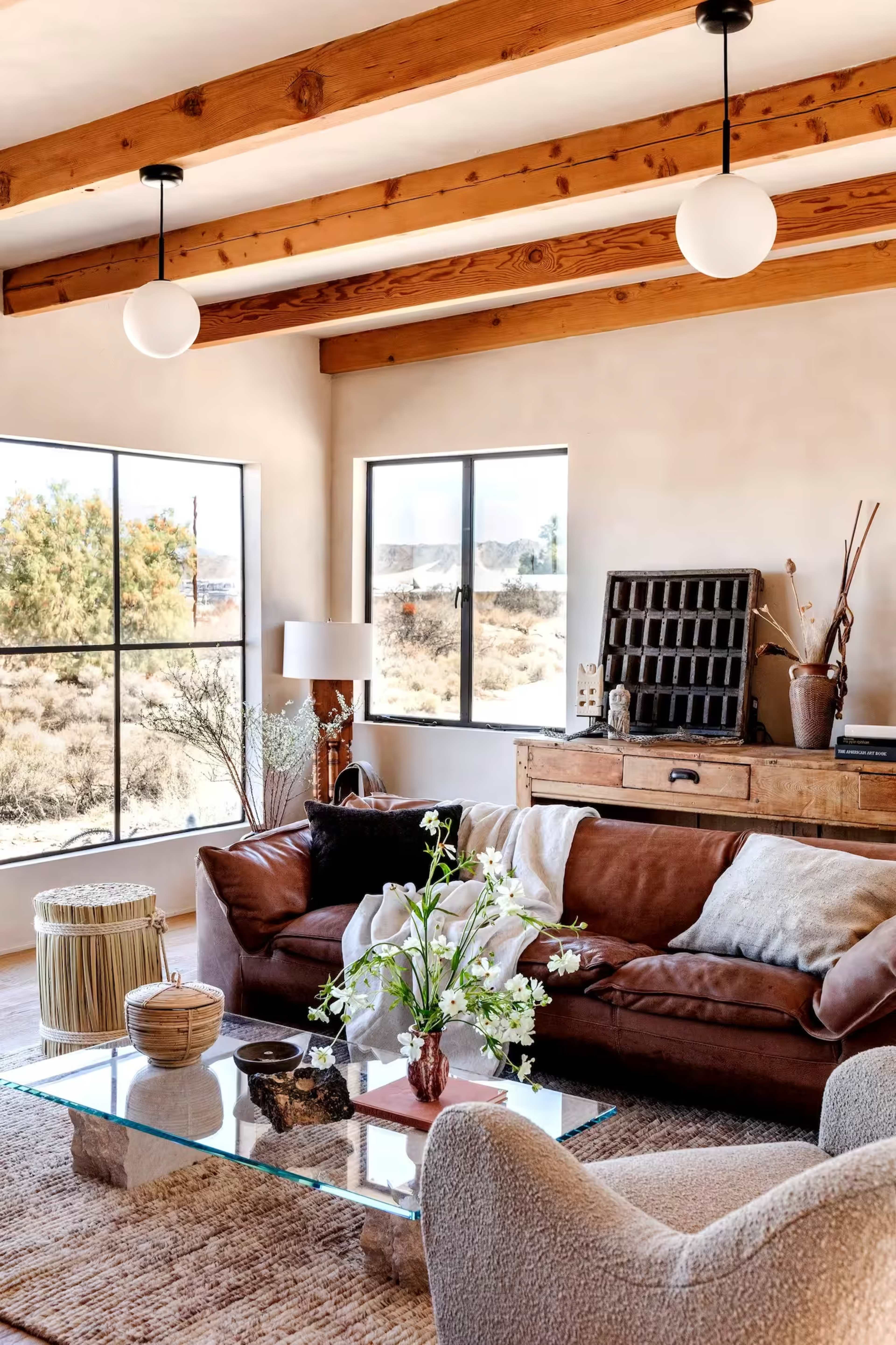 A cozy living room features a brown leather sofa, glass coffee table, and large windows showcasing a desert view.