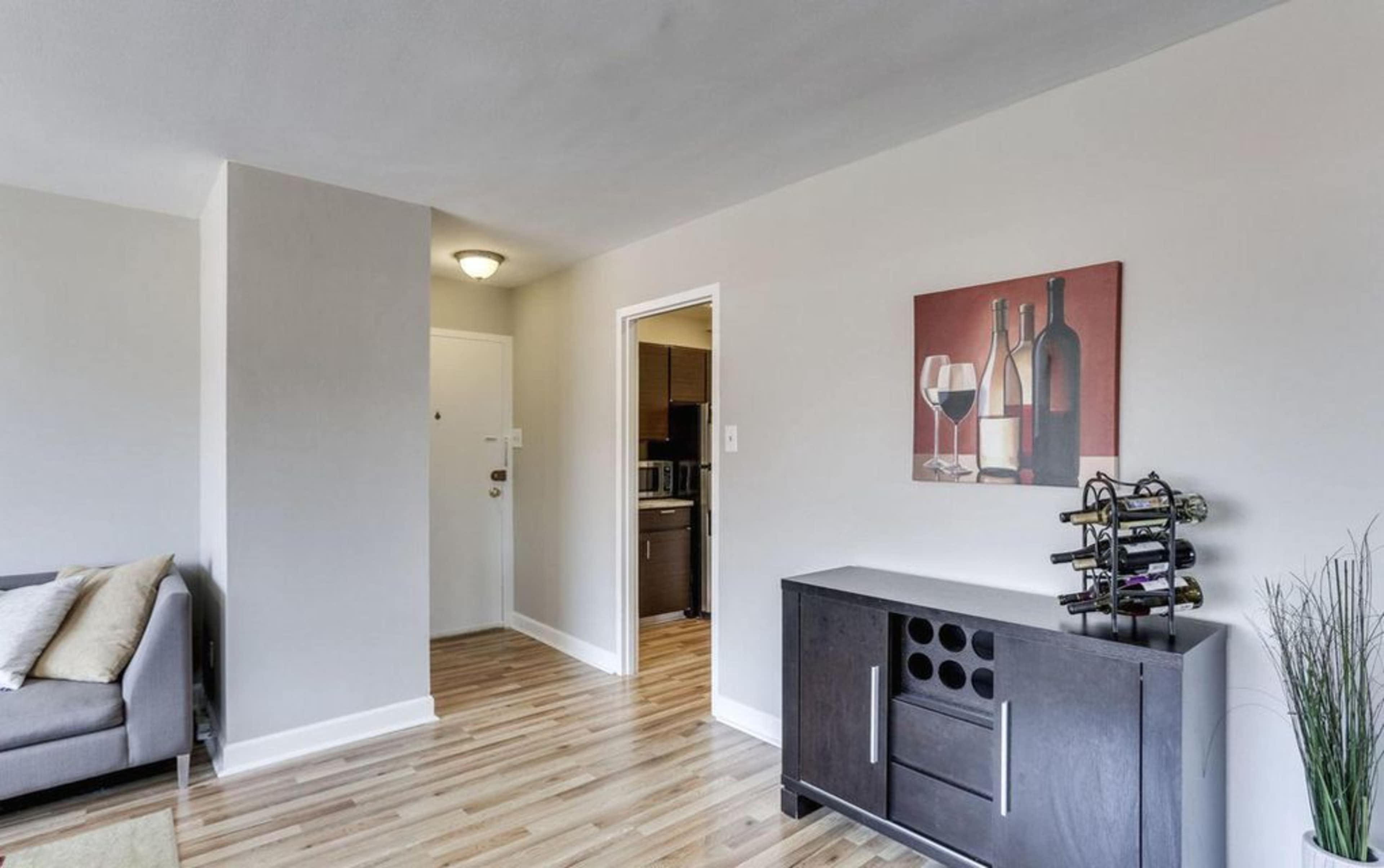 A modern living room features a gray sofa, a wine rack, and a wall art piece depicting wine bottles and glasses.