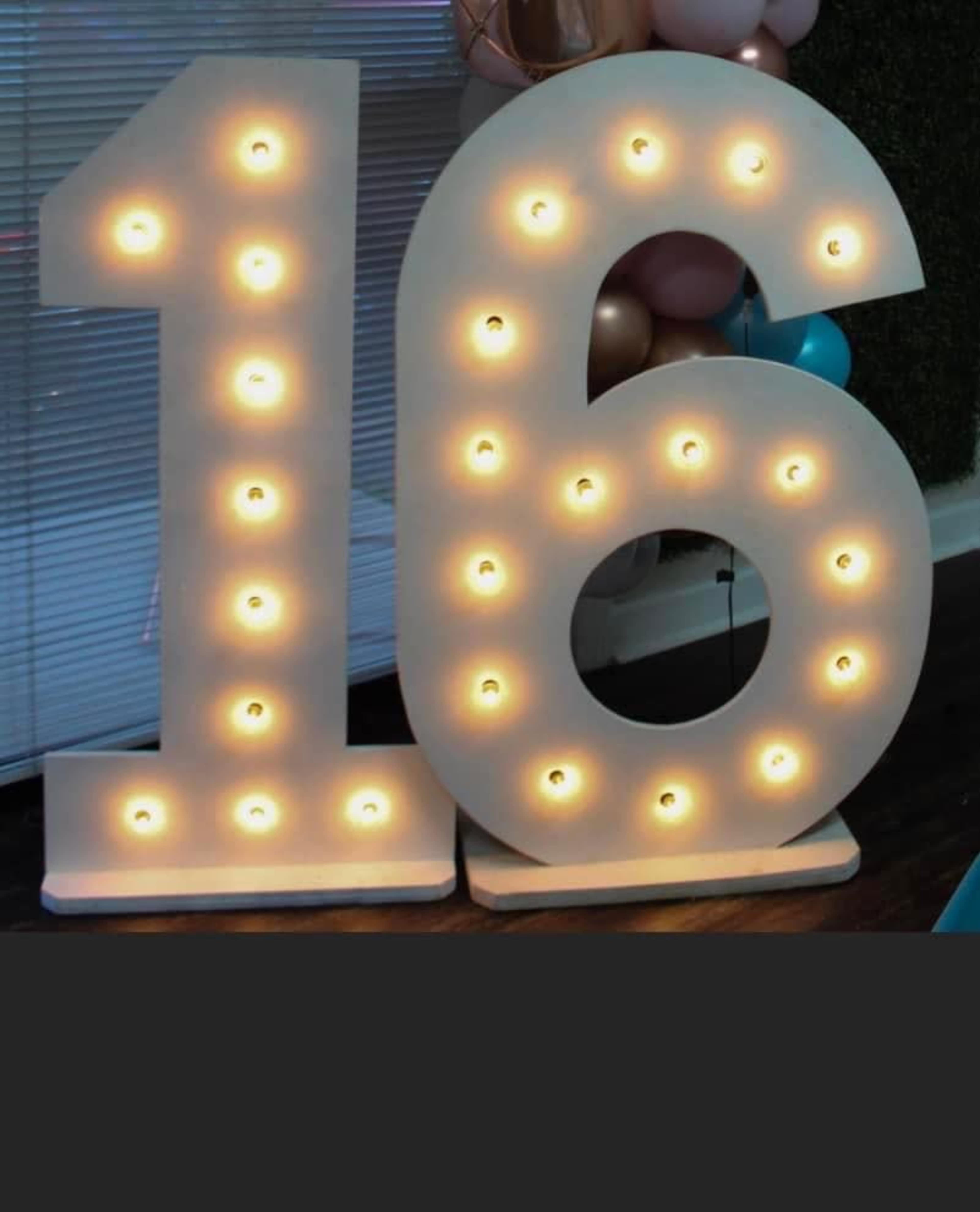 The image shows large illuminated numbers "16" made of white material with bulbs, set against a backdrop of balloons and a wall.