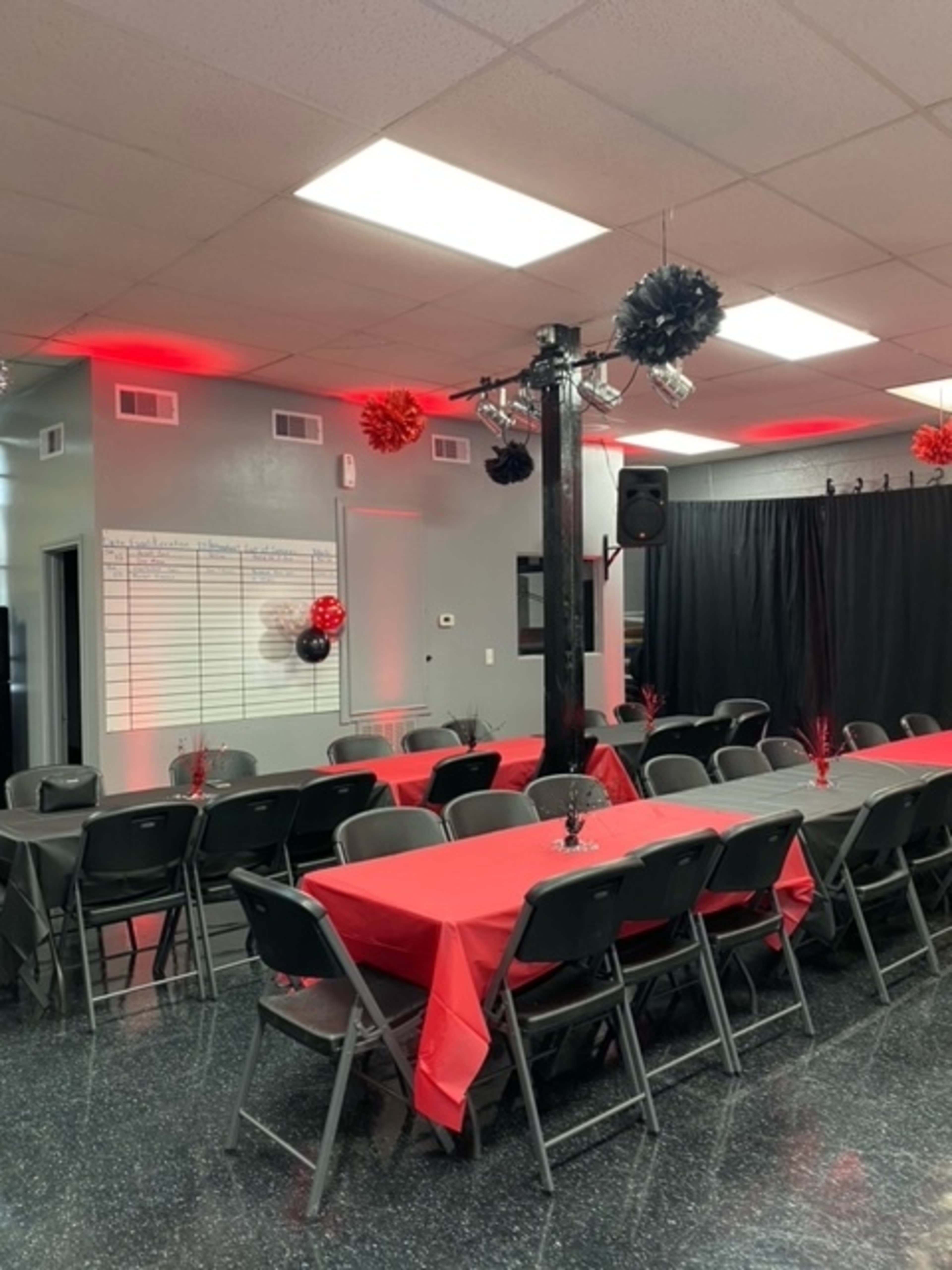 A room set up for an event, featuring several long tables covered with red tablecloths and black decorations hanging from the ceiling.
