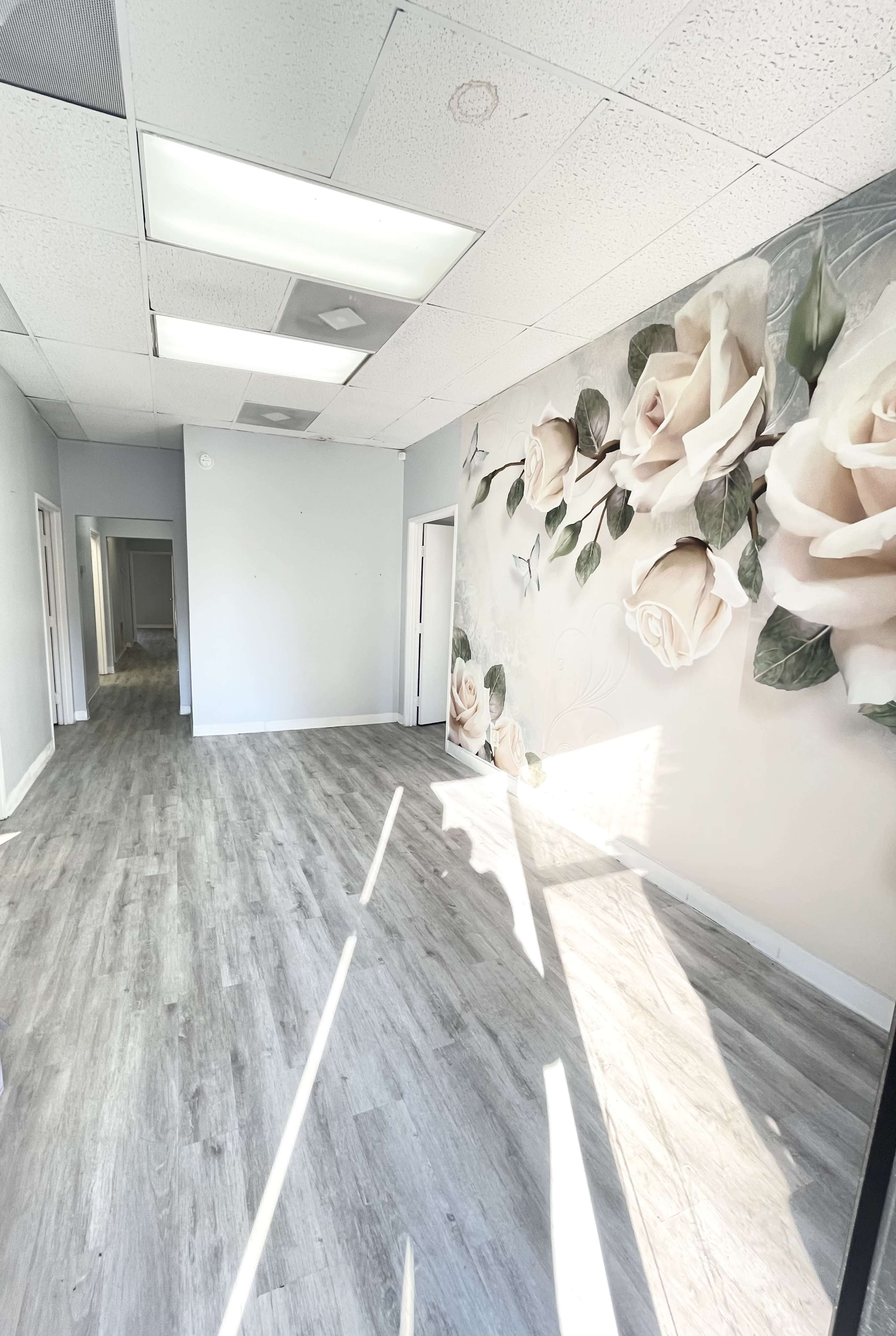 A spacious, well-lit room with gray wooden flooring and a mural of roses on one wall.