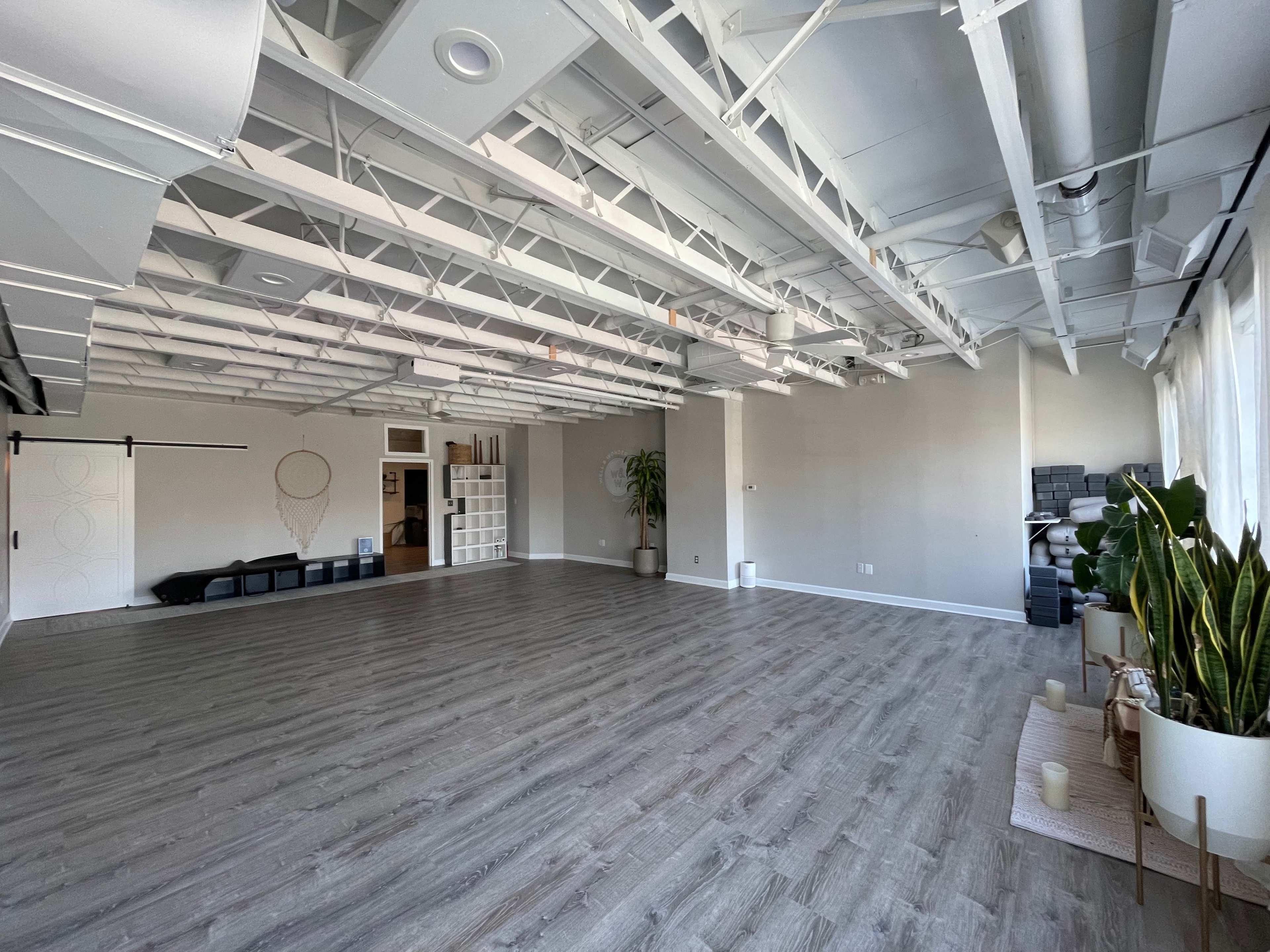 A spacious, empty room with wooden flooring, large windows, and a high ceiling featuring exposed beams.
