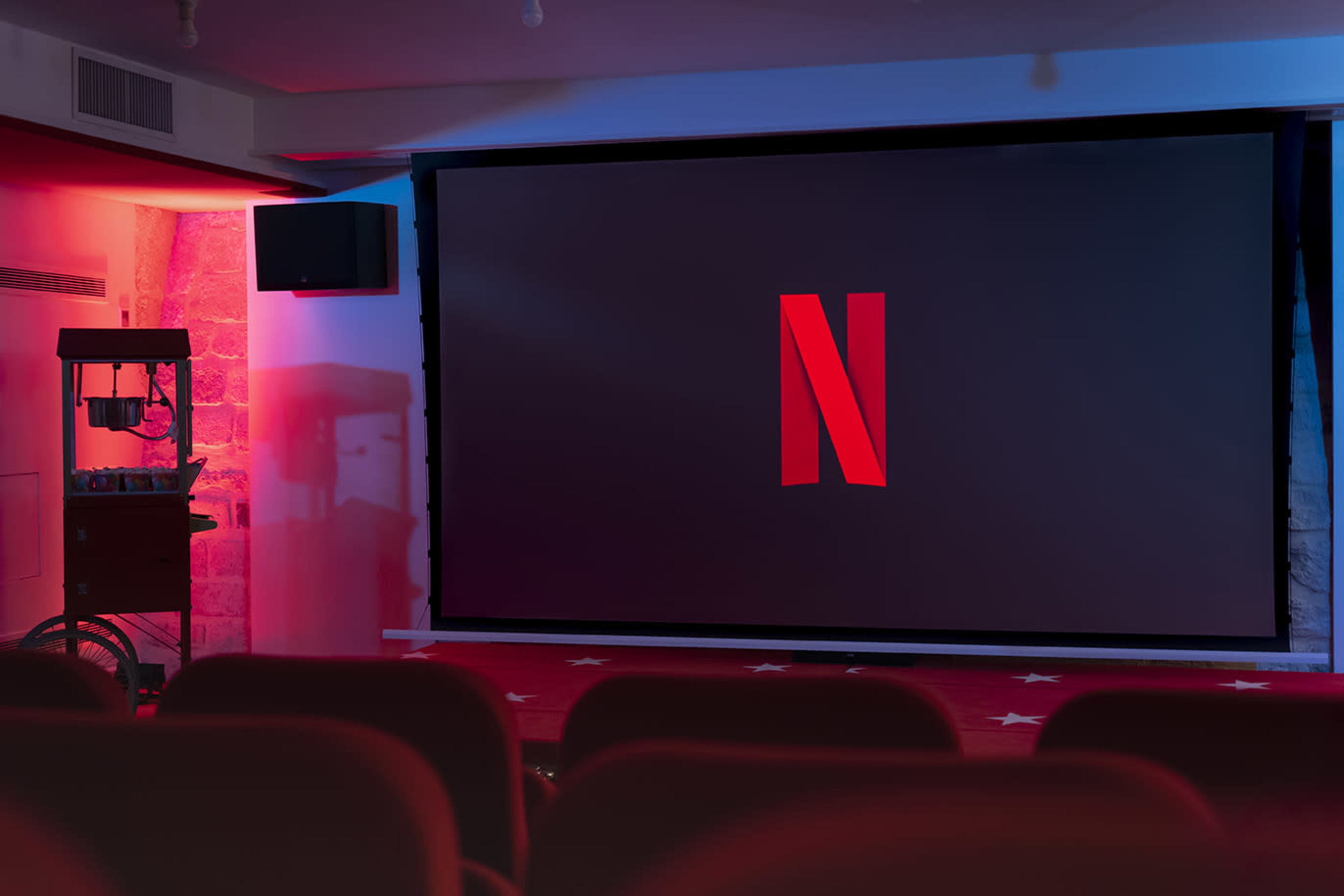 A large screen displaying the Netflix logo is set up in a dimly lit movie theater with red seating.