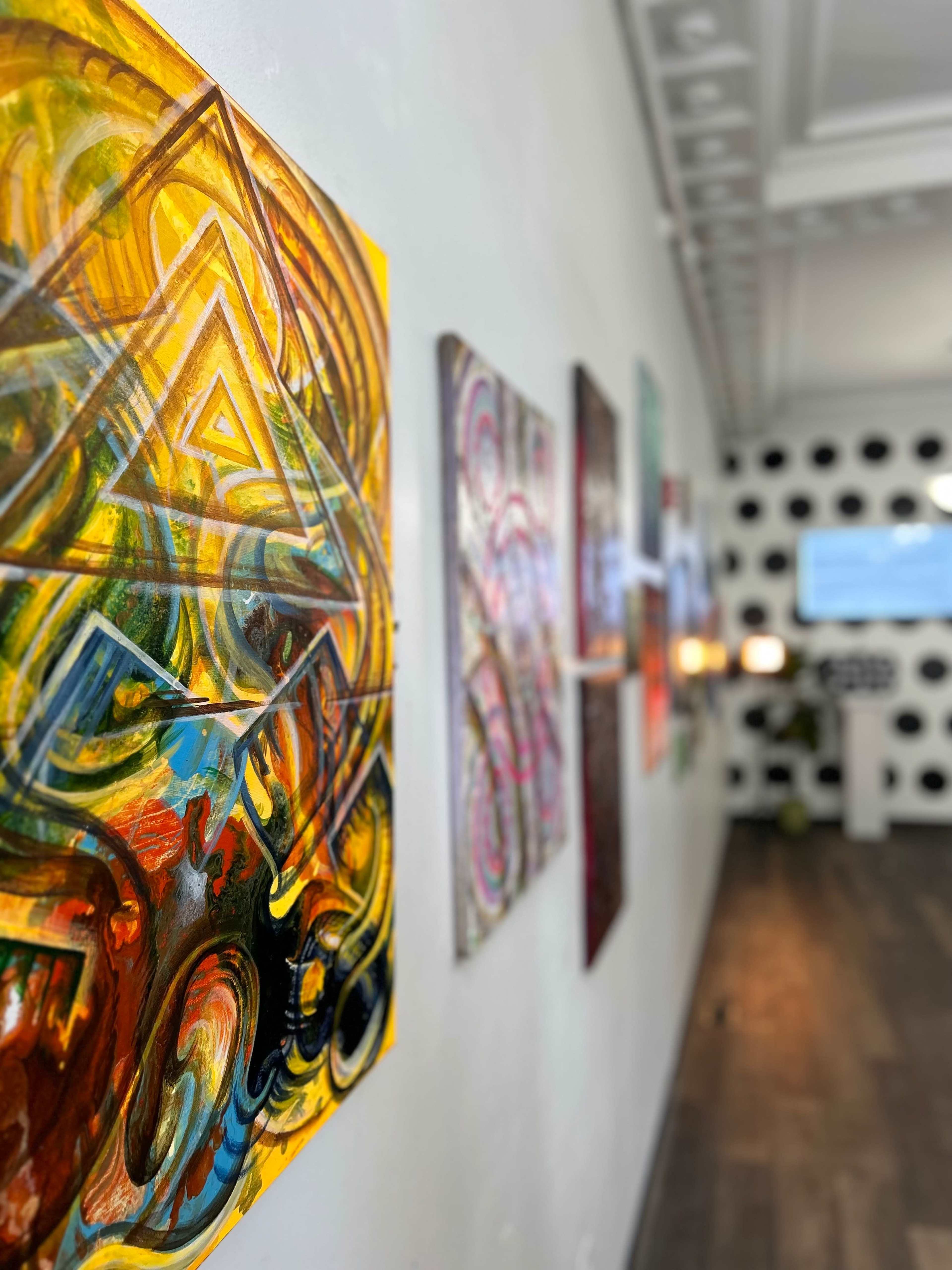 A gallery wall featuring colorful abstract paintings, with a blurred background of a room decorated with polka dots and modern furnishings.