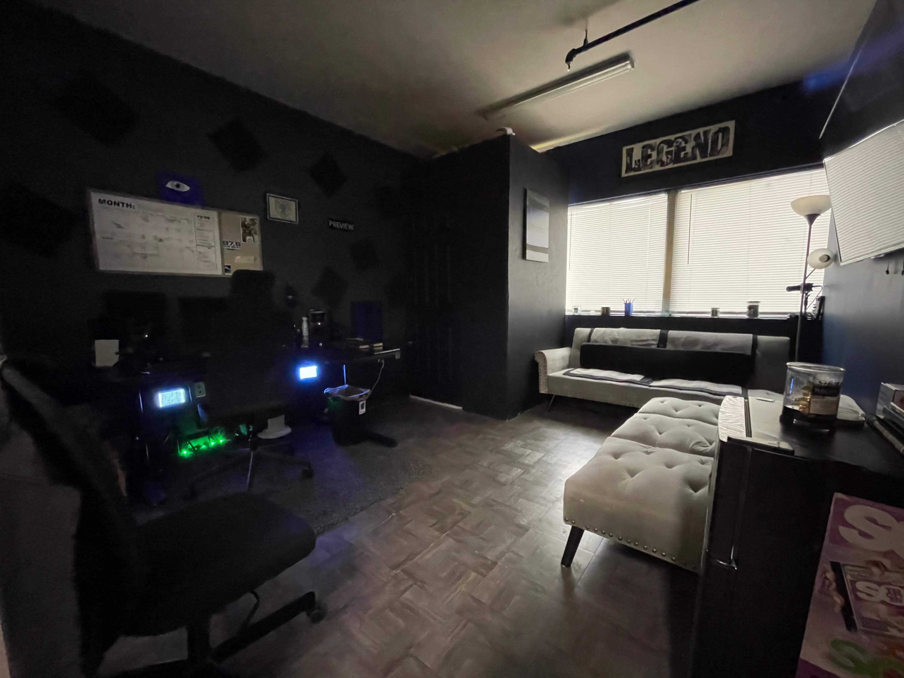 A small office space featuring dark walls, a desk with computer equipment, and a white couch against the wall.